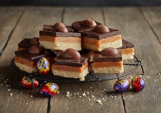 Millionaire's shortbread squares stacked up on cooling rack with creme eggs
