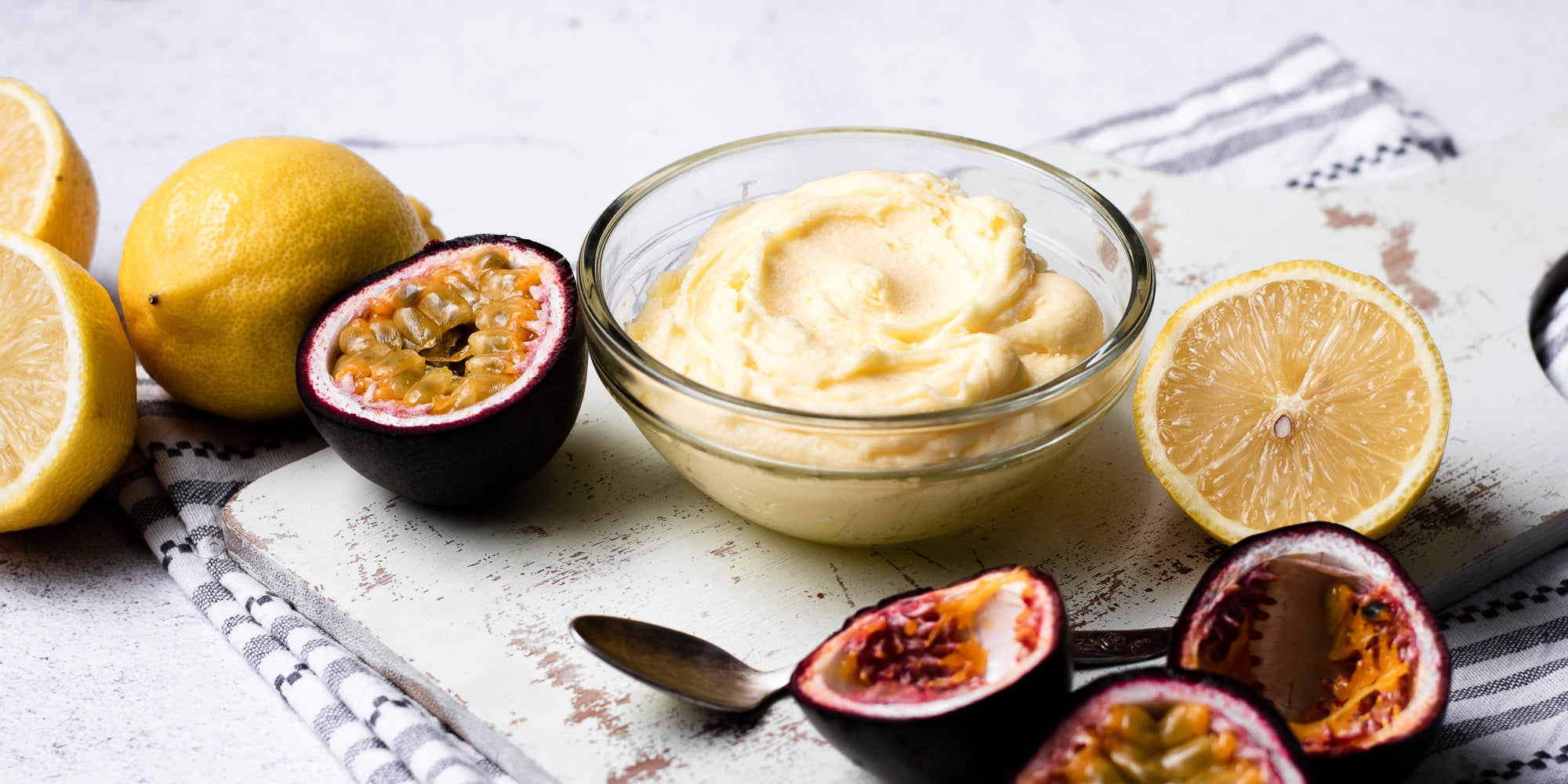 A glass bowl of Passion fruit Icing with slices of passion fruit and lemons on a serving board