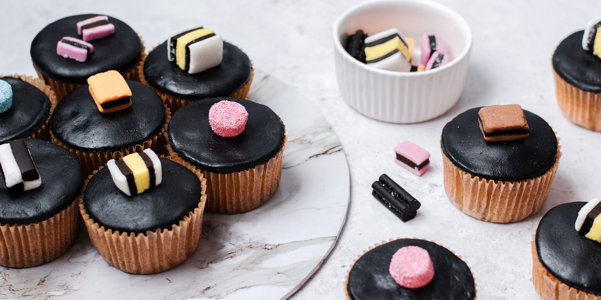 Cupcakes in brown cases, black fondant, topped with liquorice allsorts. Bowl of sweets 