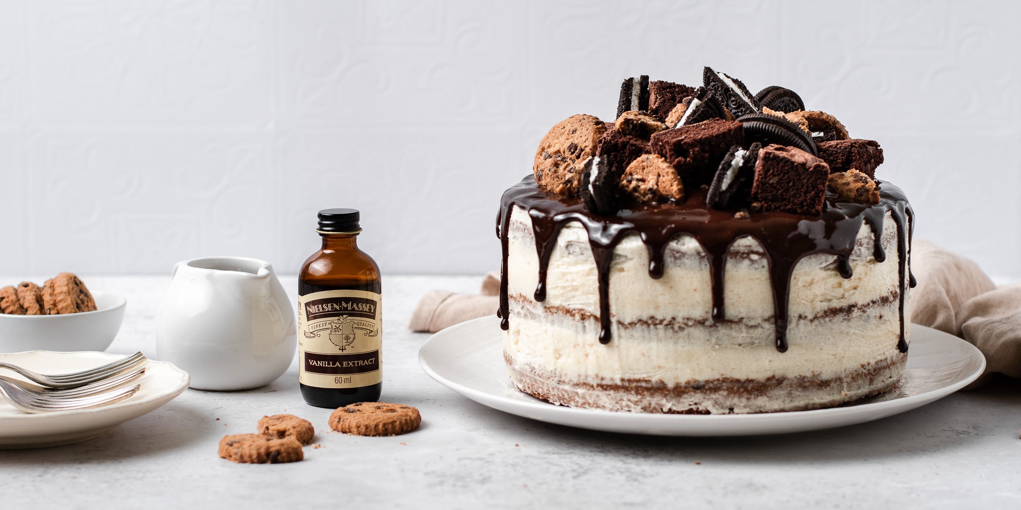 Cookie, Oreo & Brownie Layered Cake with chocolate drip, next to a bottle of Neilsen-Massey vanilla extract