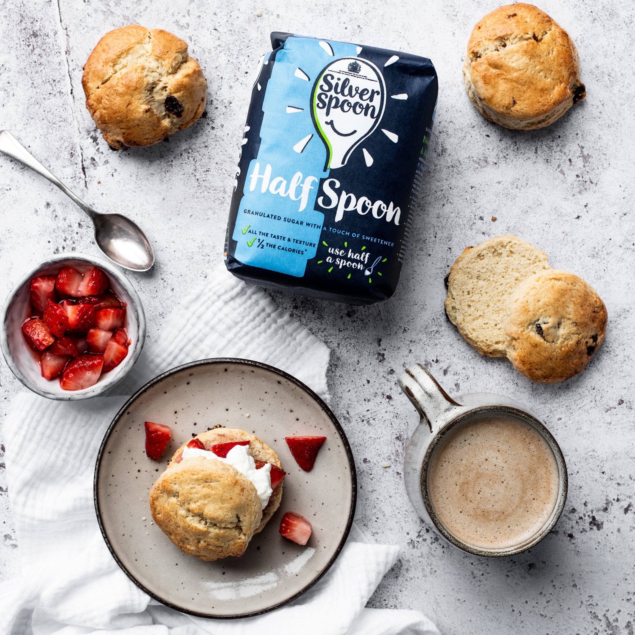 scone with strawberries and cream on a plate with silver spoon half sugar