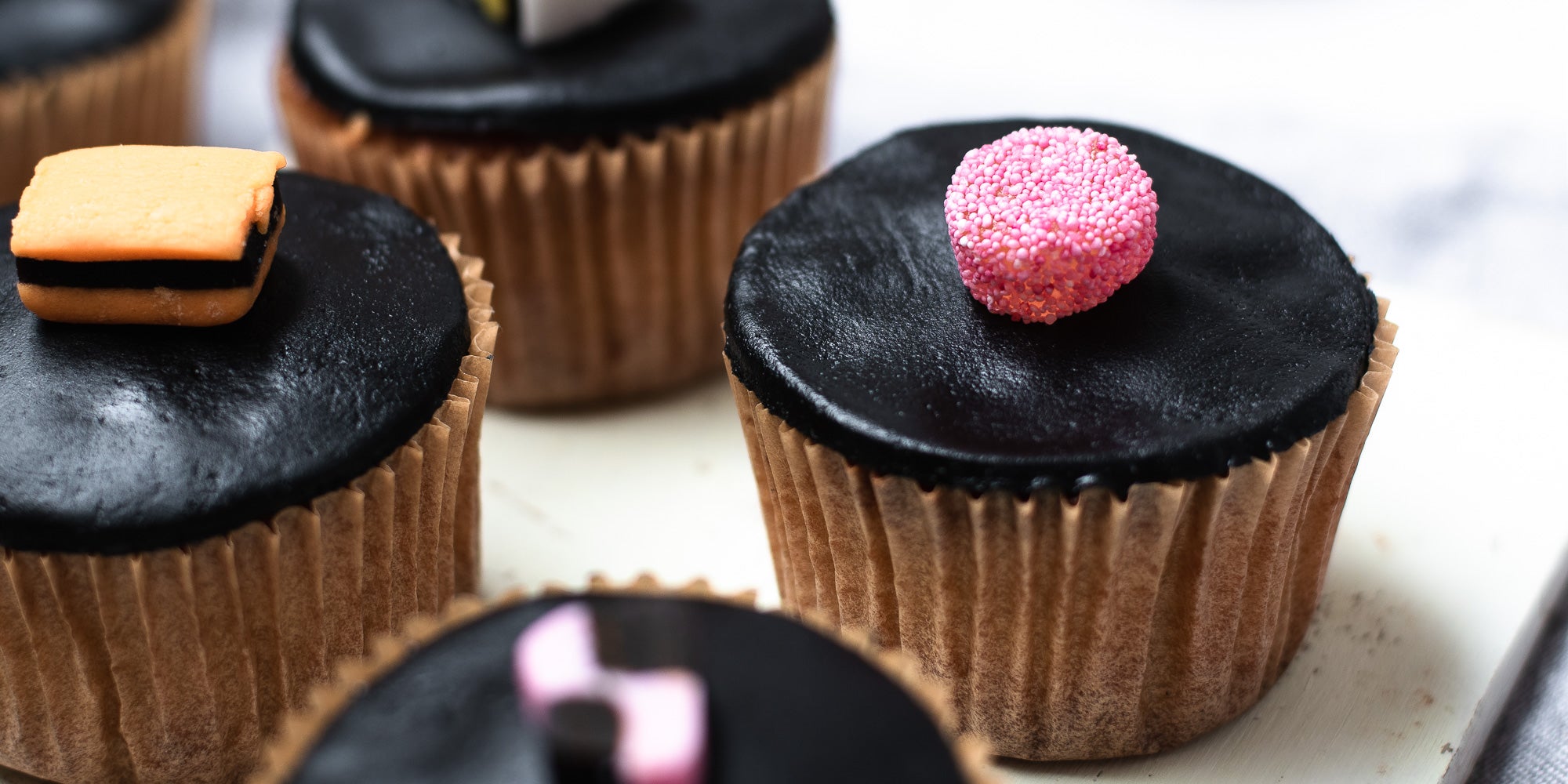 Close up of cupcakes in brown cases, black fondant, topped with liquorice allsorts