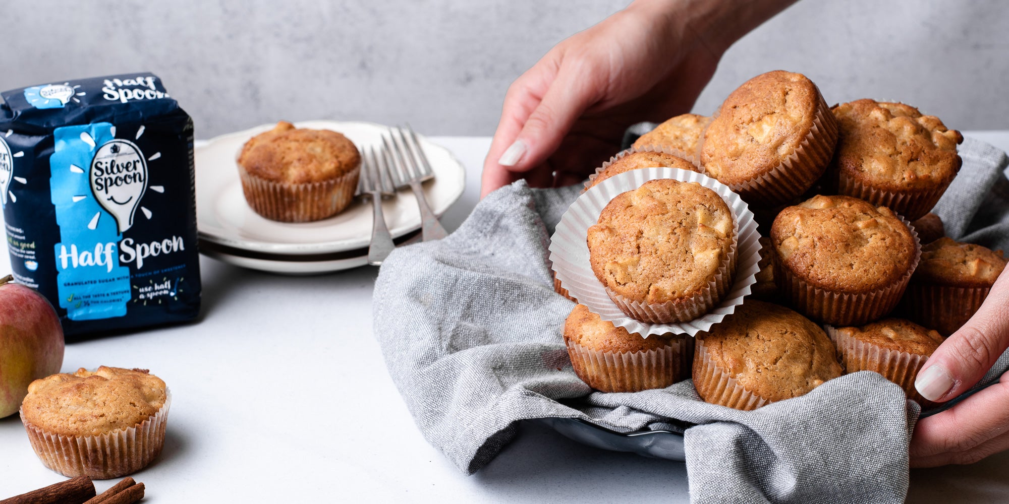 Calorie Conscious Apple & Cinnamon Muffins being held on a plate, with a bag of Silver Spoon Half Spoon sugar