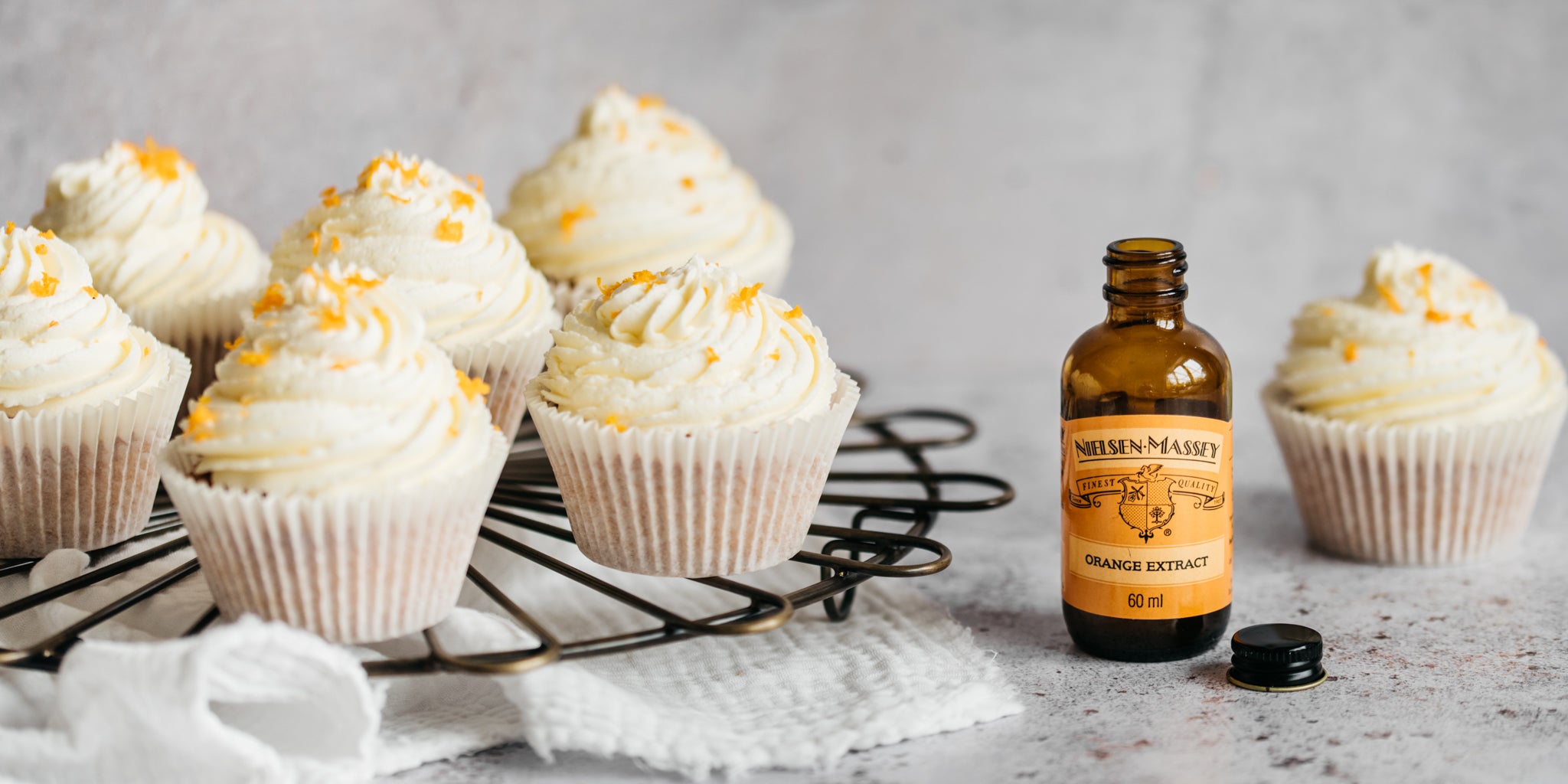Orange Blossom Cupcakes on a wire rack next to a bottle of Nielsen Massey Orange Blossom Extract