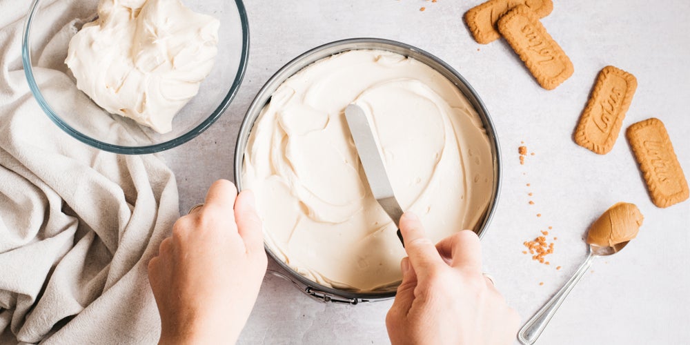 Hand spreading cheesecake mix into a tin