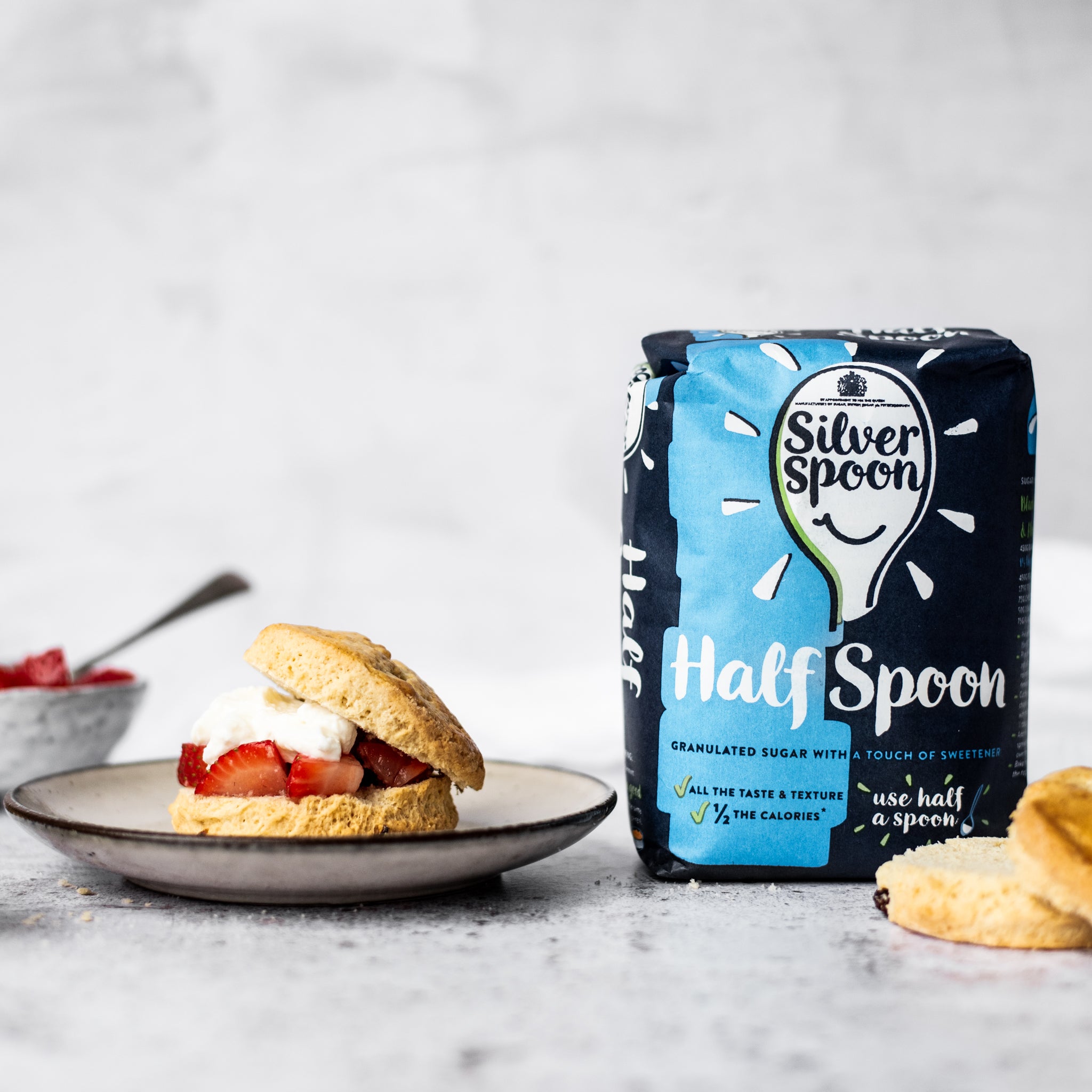 scone with strawberries and cream on a plate with silver spoon half sugar