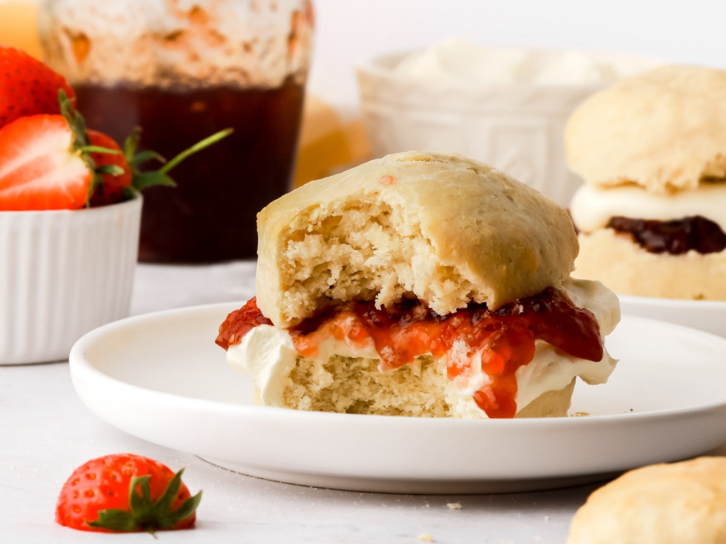 Close up of a scone filled with cream and strawberry jam, surrounded by strawberries