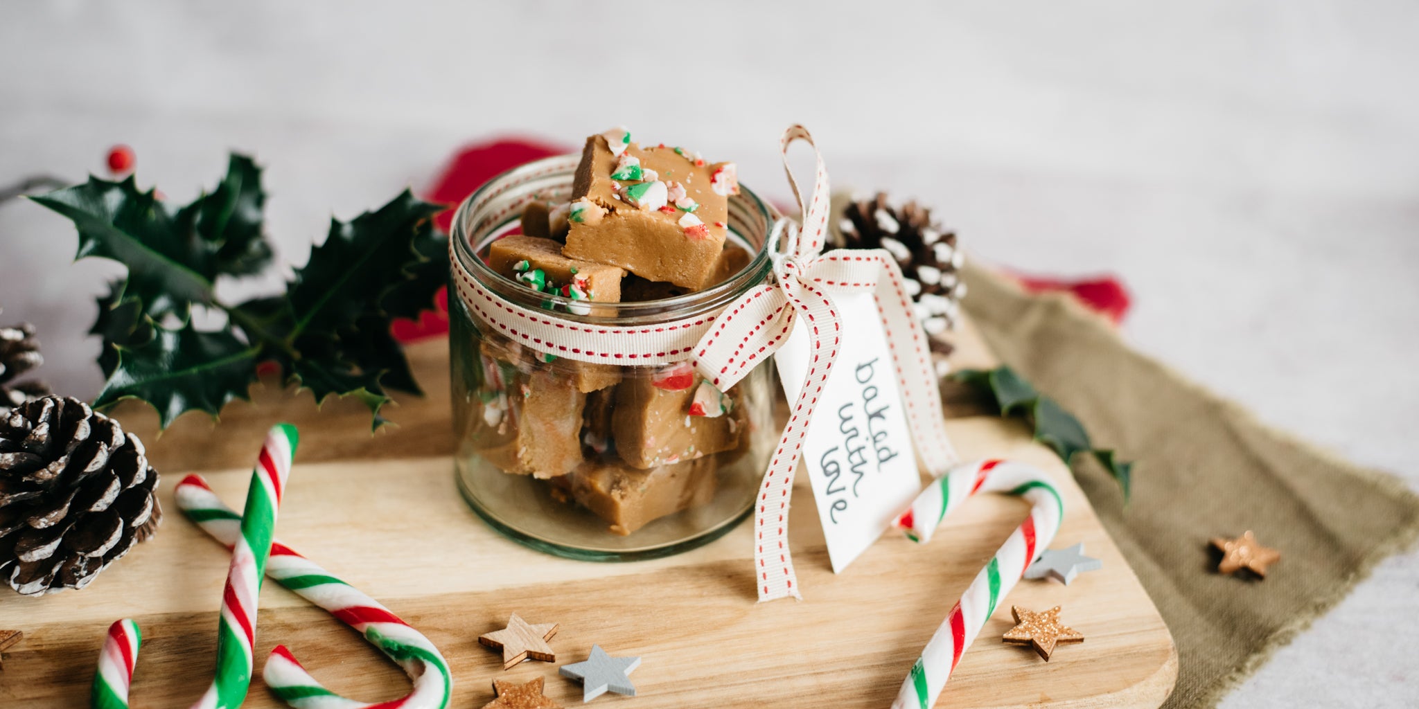 Candy Cane Fudge in a jar with a hand tied gift tag, surrounded by holly leaves, candy canes and ribbon