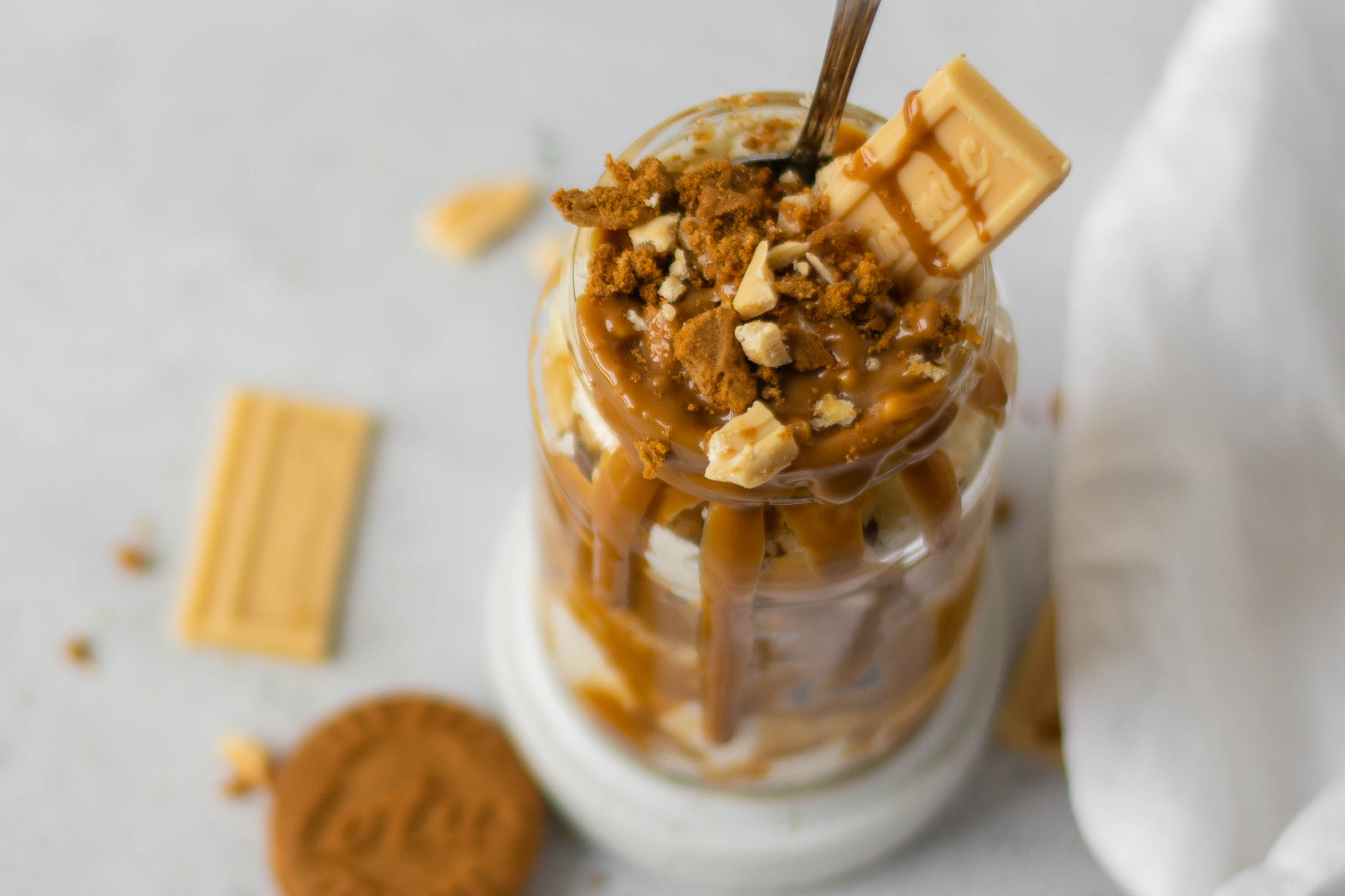Top view of Biscoff & Caramac Cake Jar topped with drizzles of Biscoff, pieces of Caramac and a spoon inside