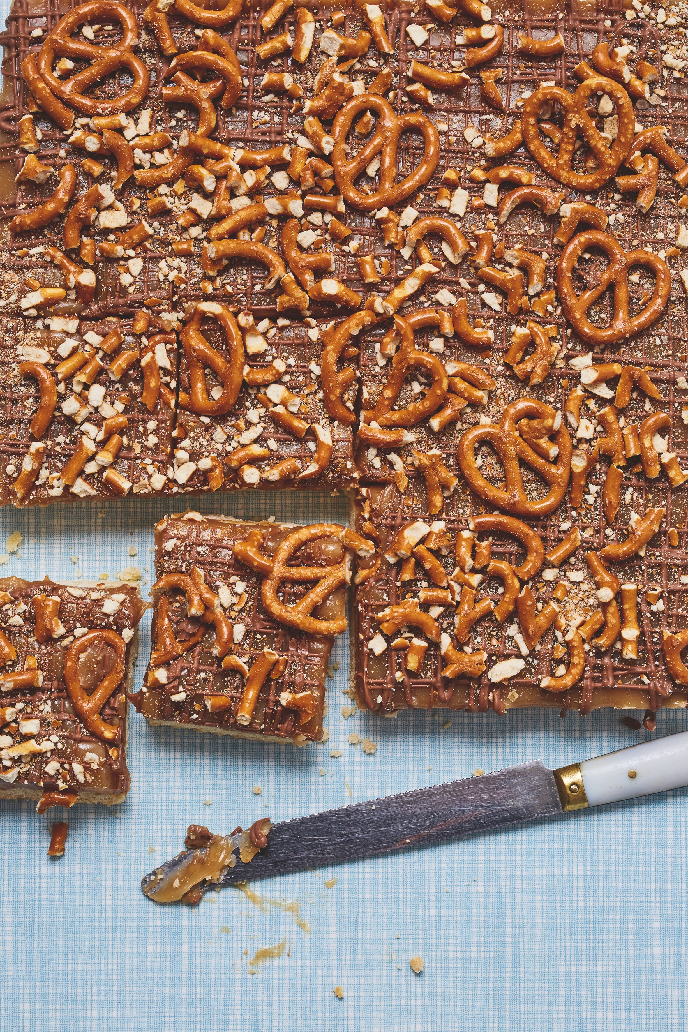 Flat lay of salted caramel pretzel slice with a knife, cuttings into squares