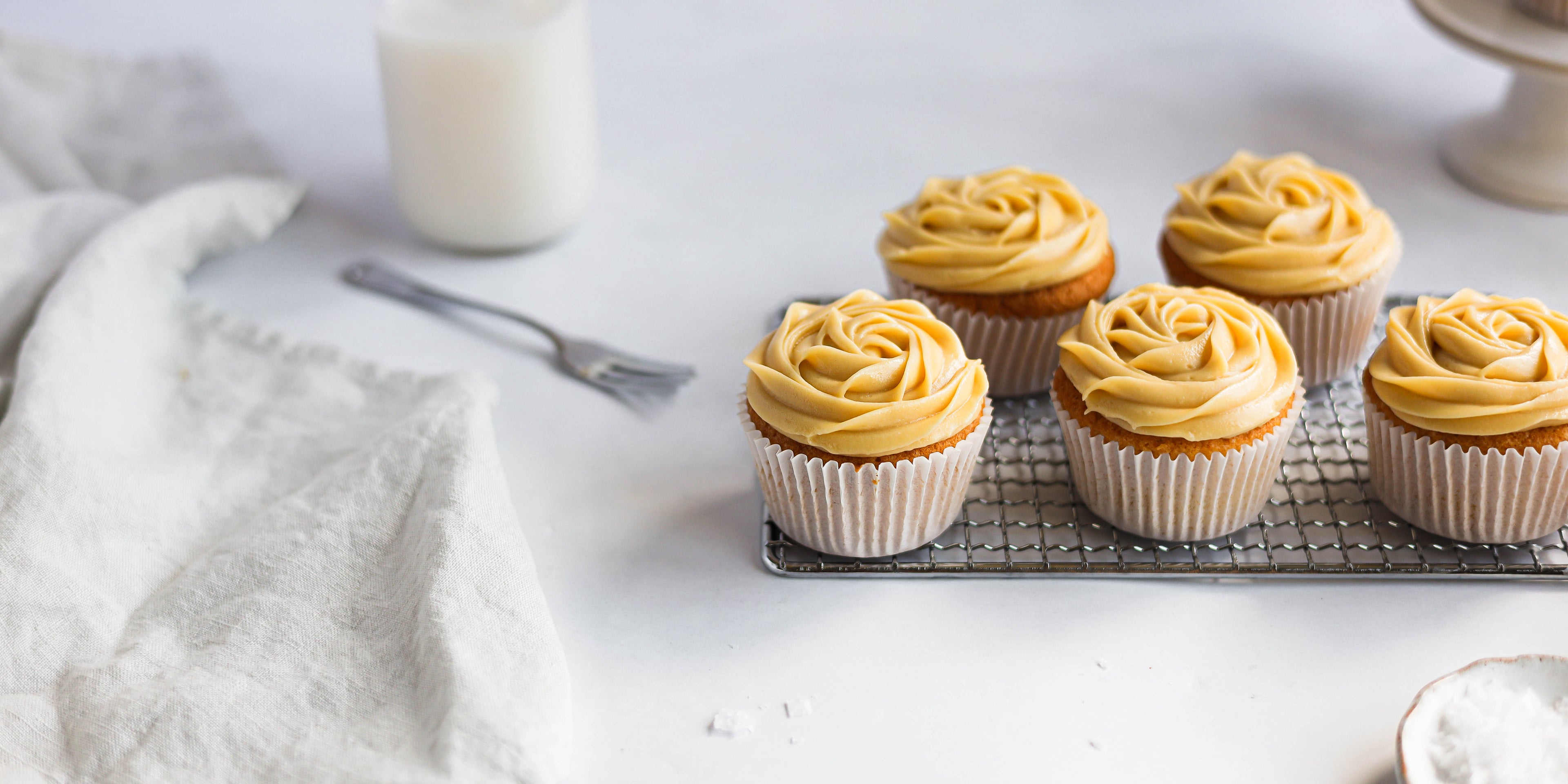 Close up of Salted Caramel Cupcakes on a wire rack with fork and glass bottle of milk in the background