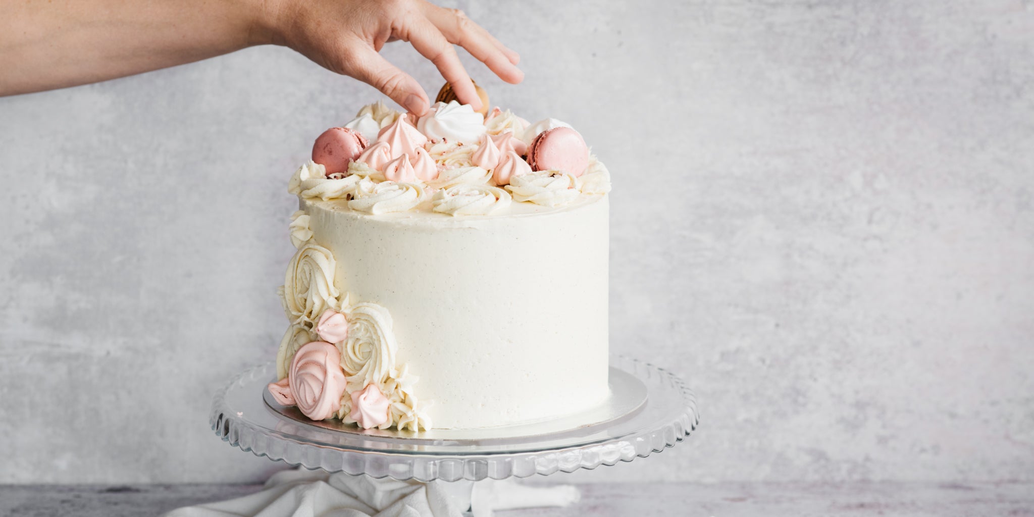 A hand adding meringues onto the top of the baking mad ultimate vanilla celebration cake 