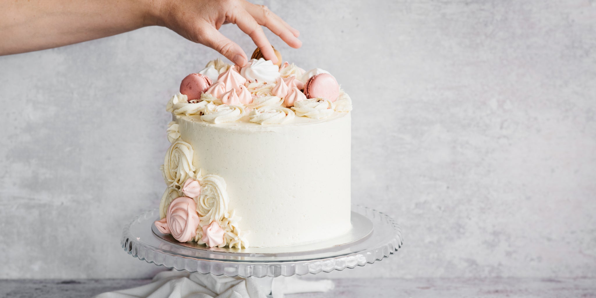 A hand adding meringues onto the top of the baking mad ultimate vanilla celebration cake