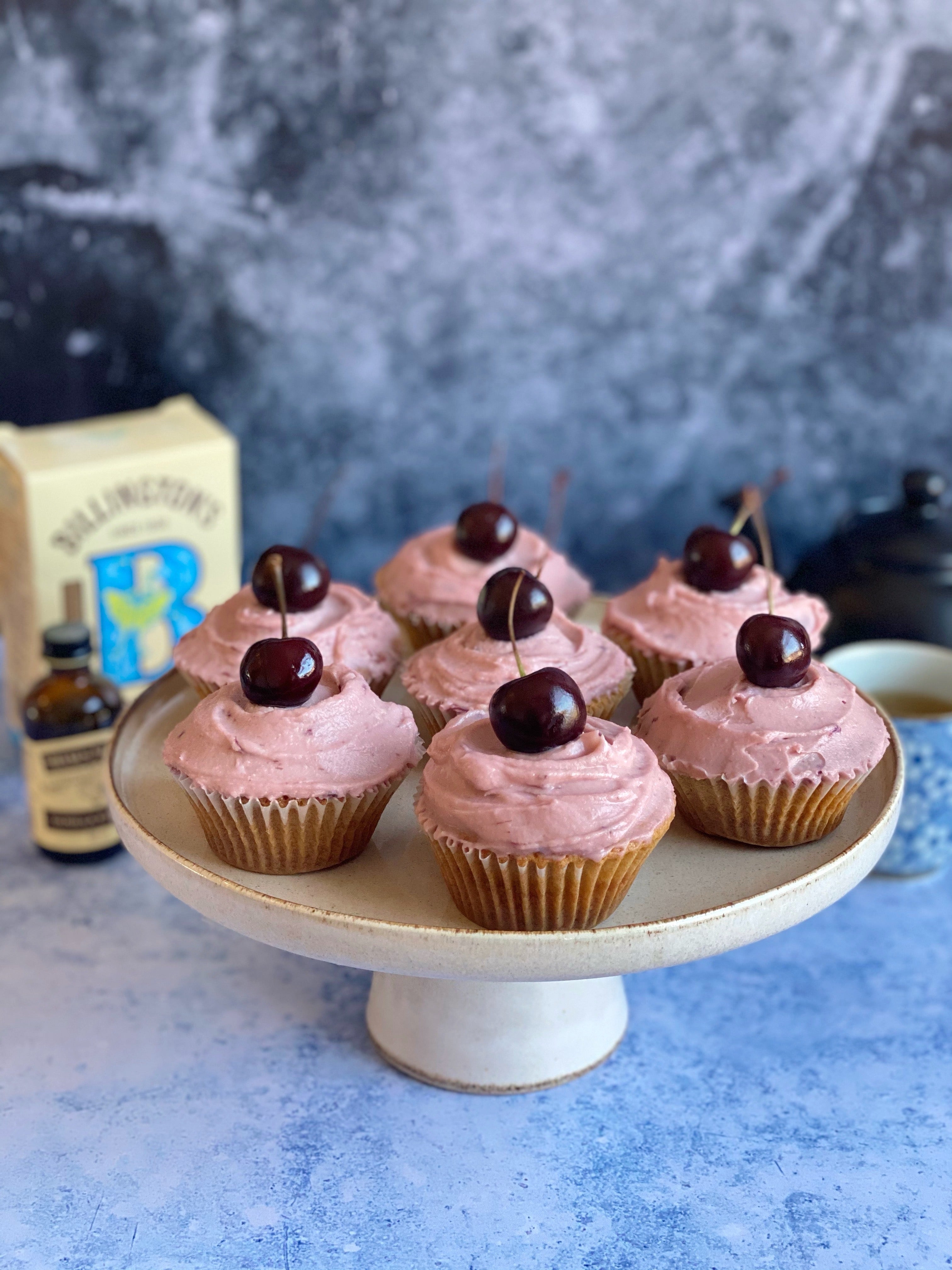 7 cupcakes with cherries on top and pink icing on cake stand