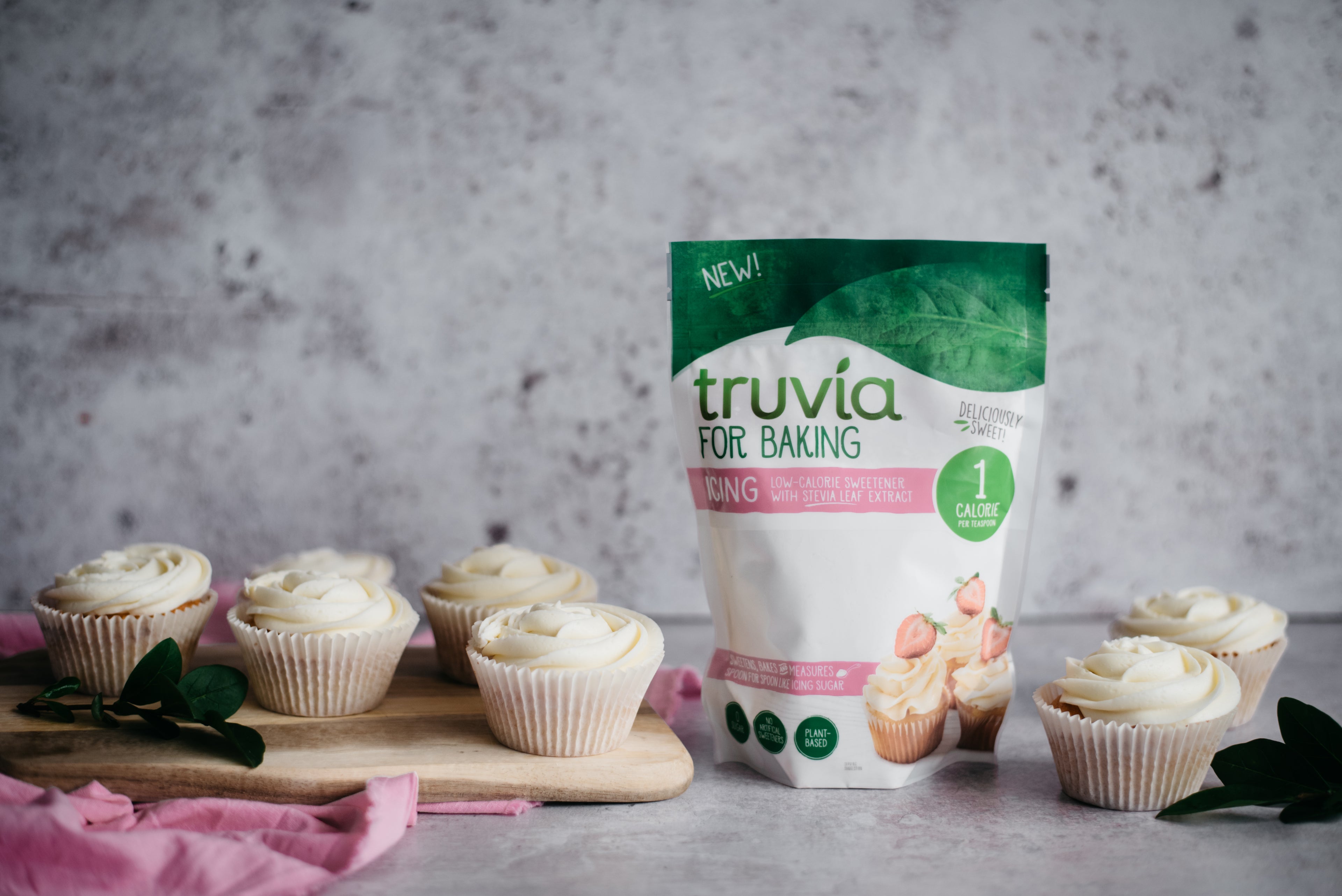 Four cupcakes covered in low sugar cream cheese frosting next to a pack of Truvia for Baking - Icing