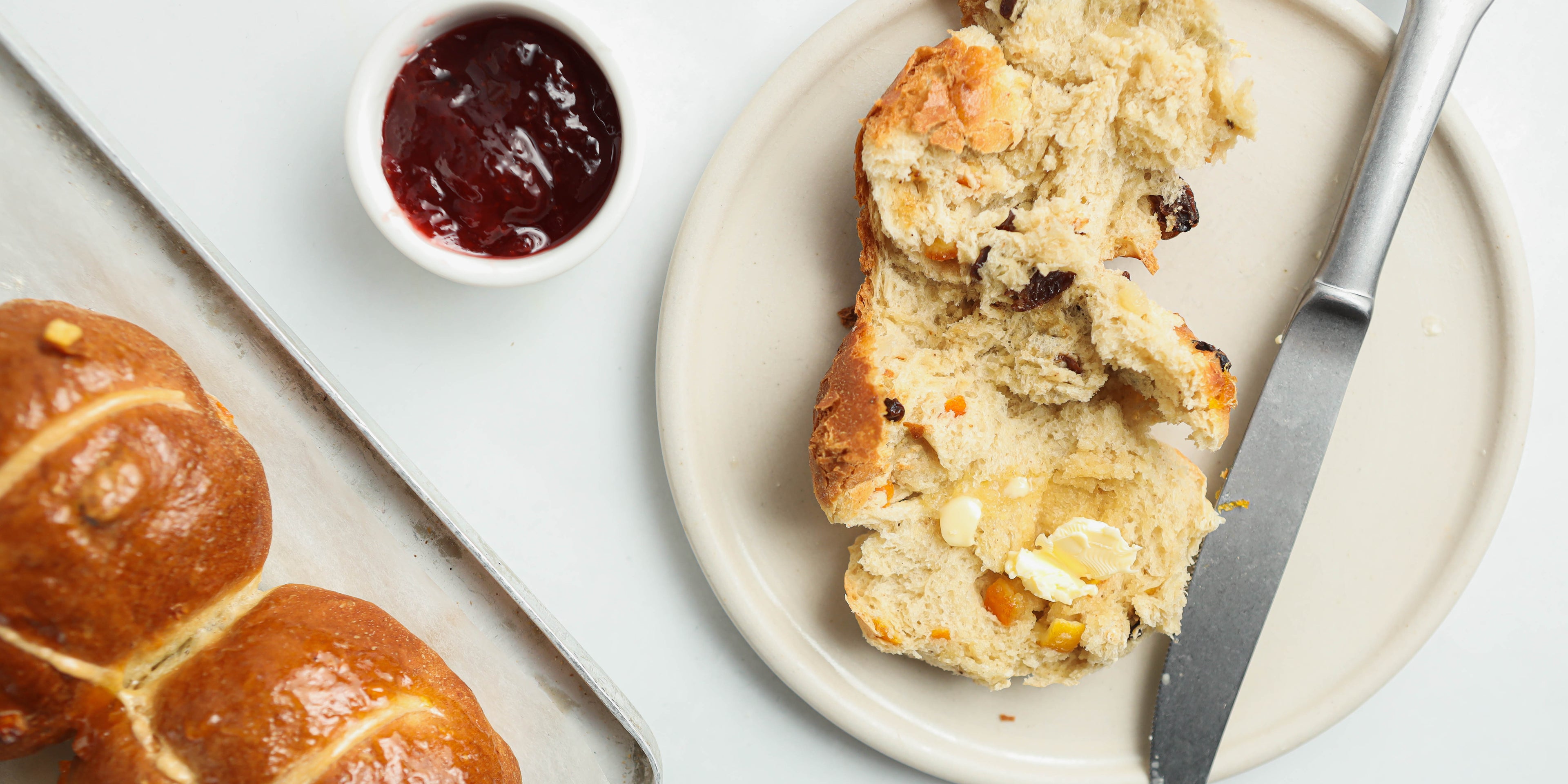 Vegan Hot Cross Buns sliced open with a knife a buttered with plant-based butter