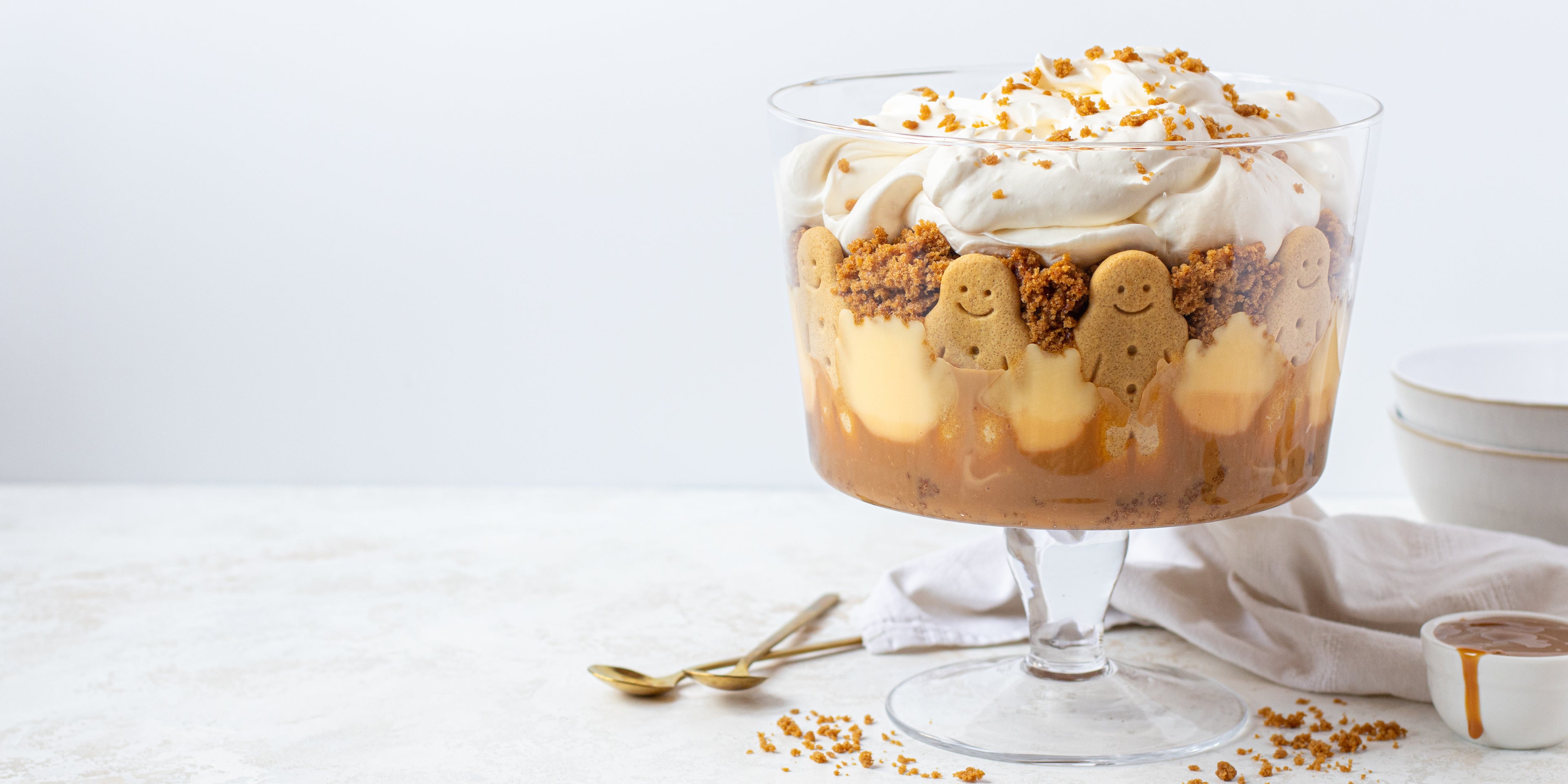 Gingerbread trifle with gingerbread men decorated around the trifle bowl, with two spoons ready to serve