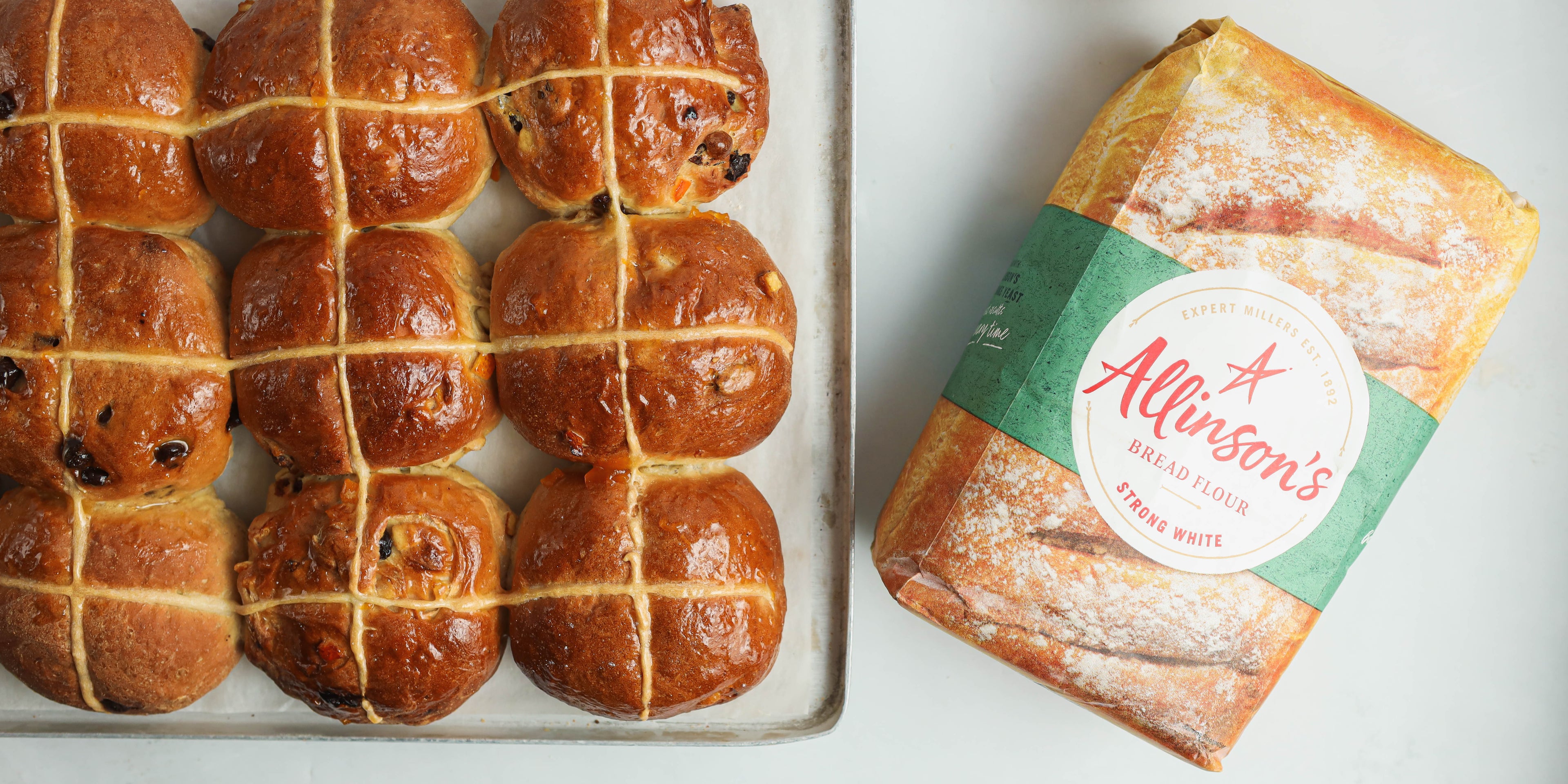 Top view of a fresh batch of Vegan Hot Cross Buns next to a bag of Allinson's Strong White flour