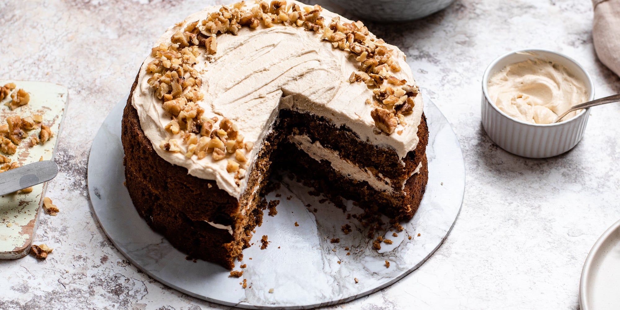 Close up of a Gluten Free Vegan Coffee Cake with a slice cut out of it showing the insides. Next to a ramekin of buttercream
