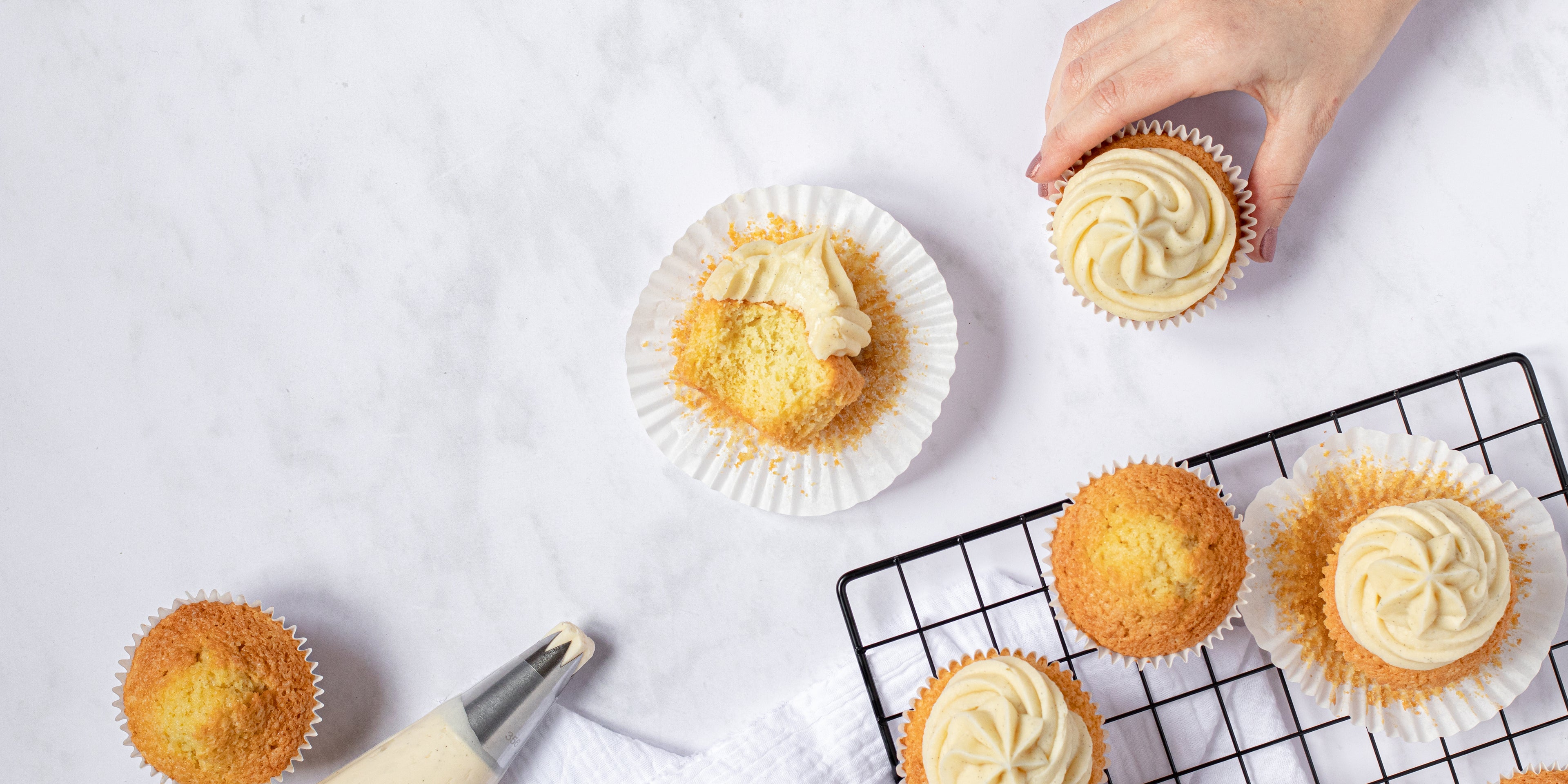Vanilla cupcakes on a baking tray and table topped with vanilla buttercream