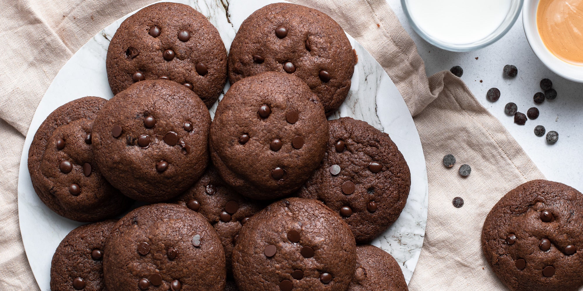 A batch of Chocolate & Peanut Butter Stuffed Cookies with chocolate chips and a glass of milk