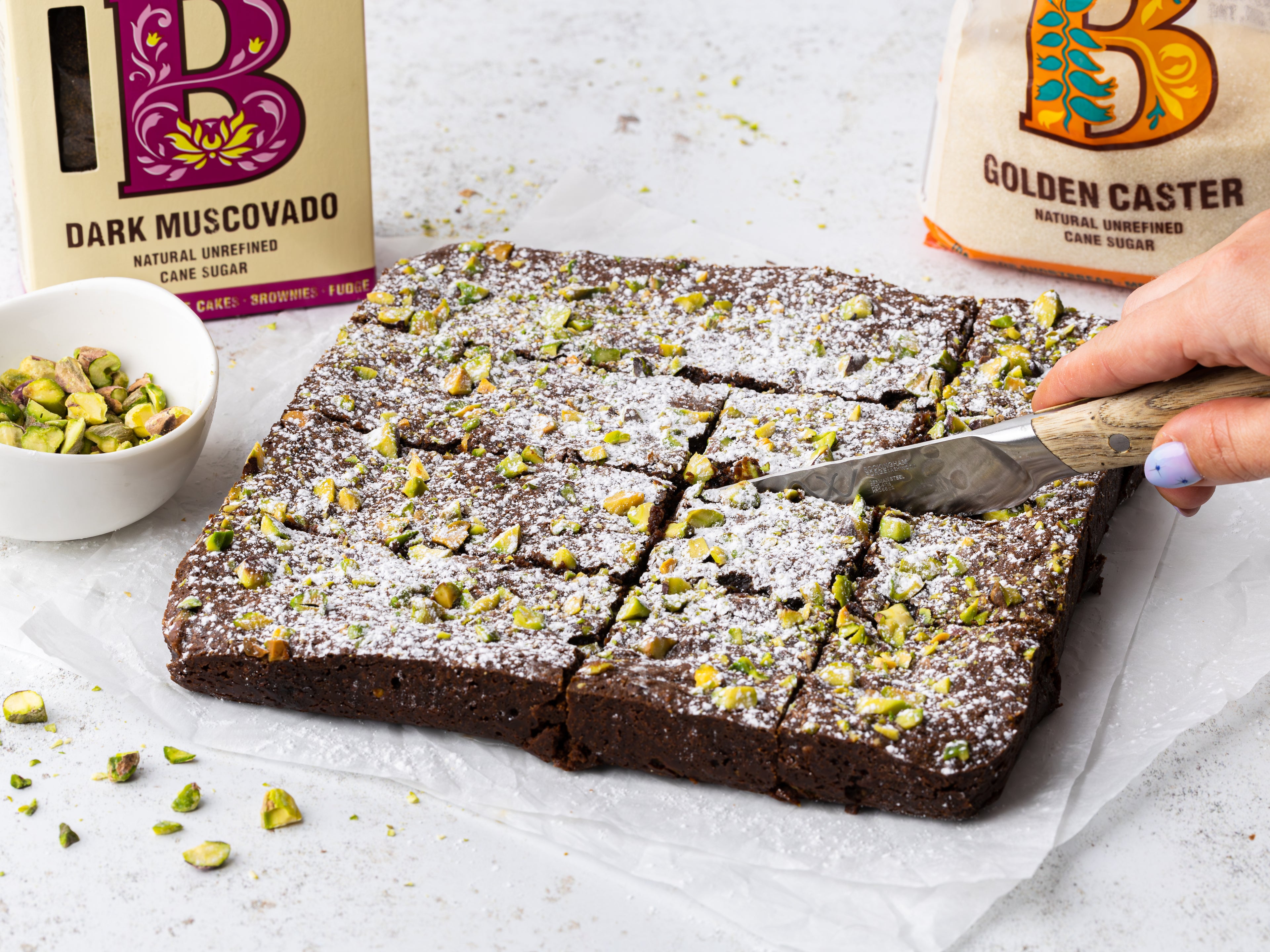 Brownies being cut up into squares and topped with pistachios