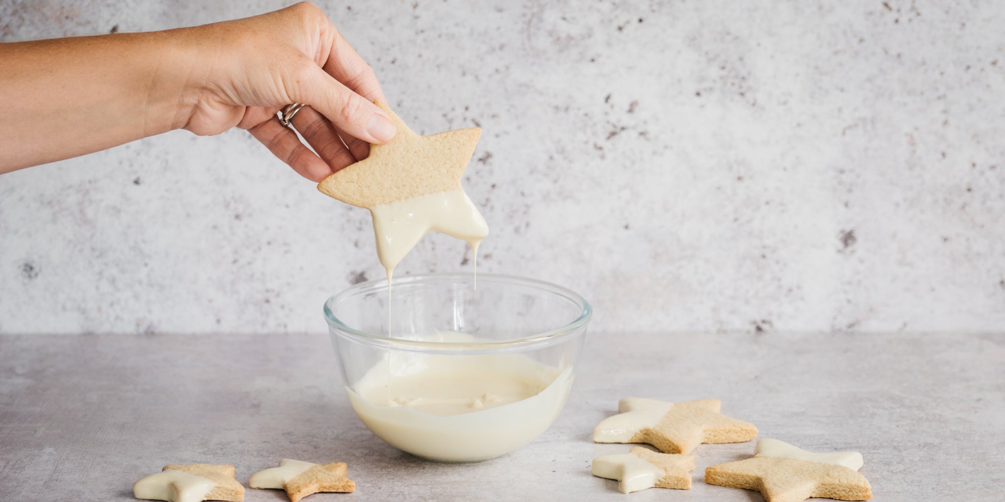 Hand dipping star biscuits into a glass bowl of melted white chocolate