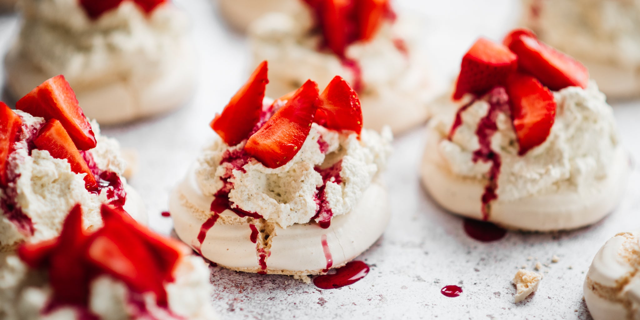 Three meringue nests topped with crushed meringues and strawberry slices and a drizzle of strawberry sauce