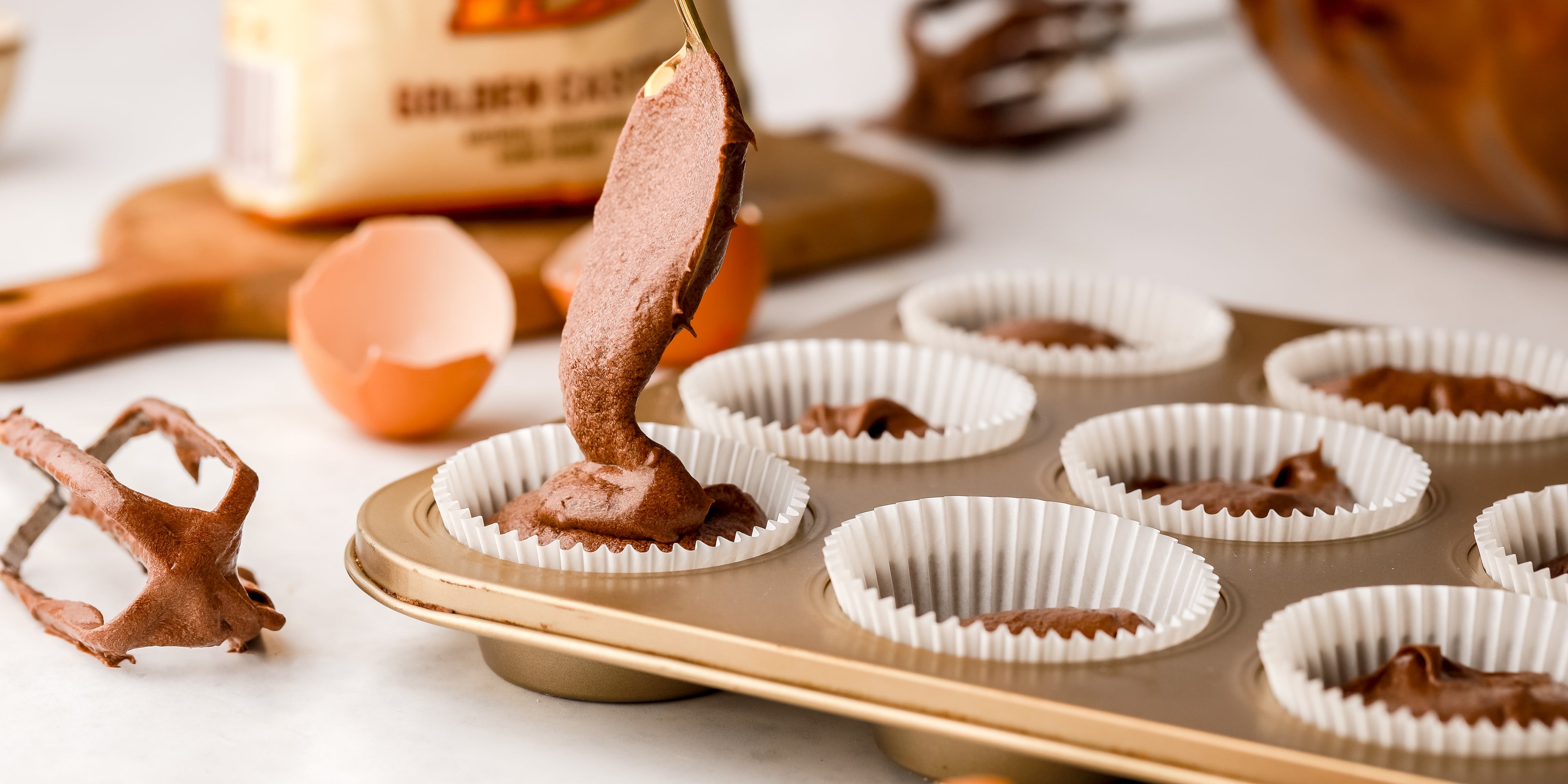 Chocolate cupcake batter being spooned into paper cake cases