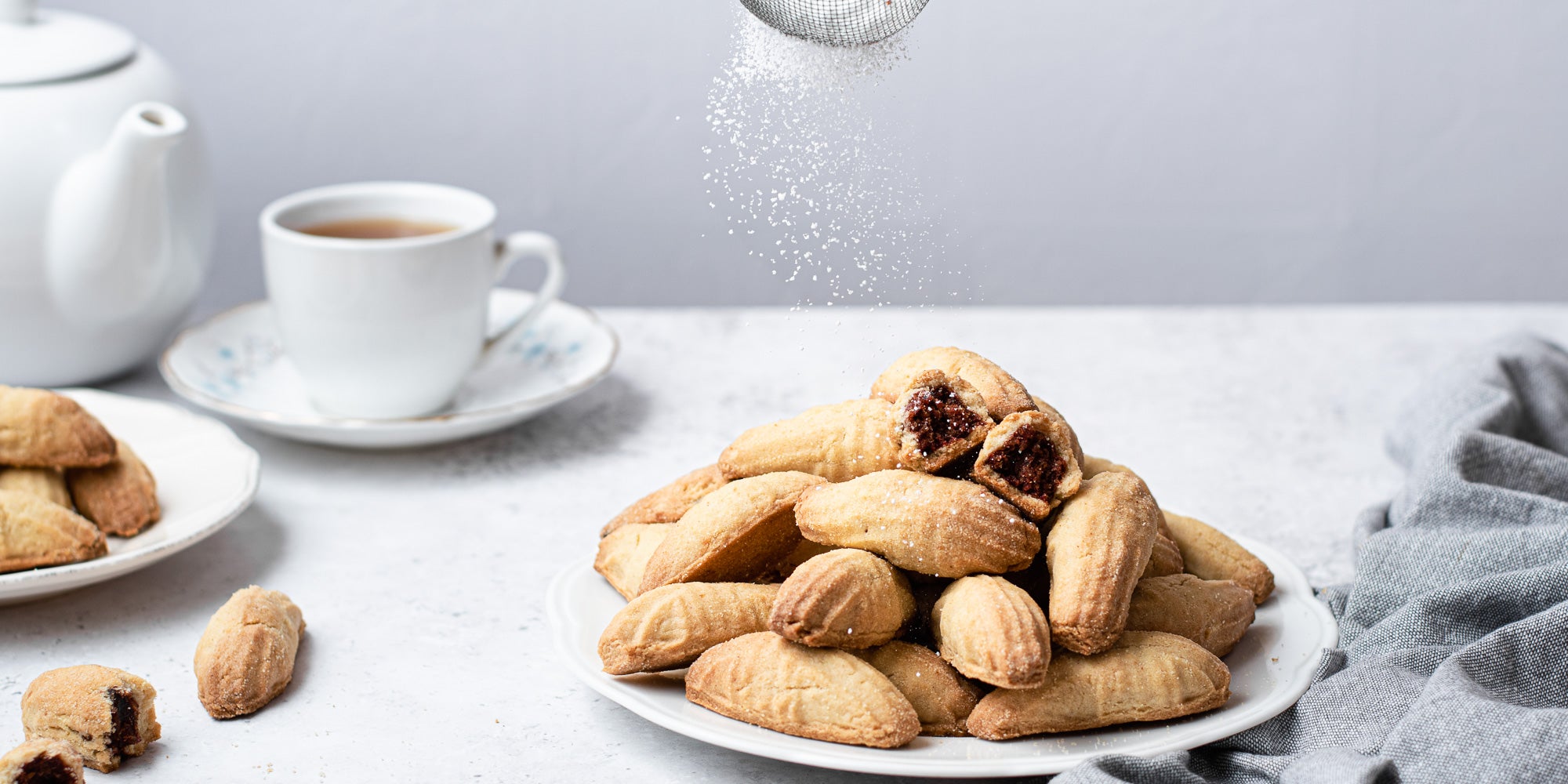 Two plates of Mamoul cookies on white plates, cup of tea in background and icing sugar dusted on top. 