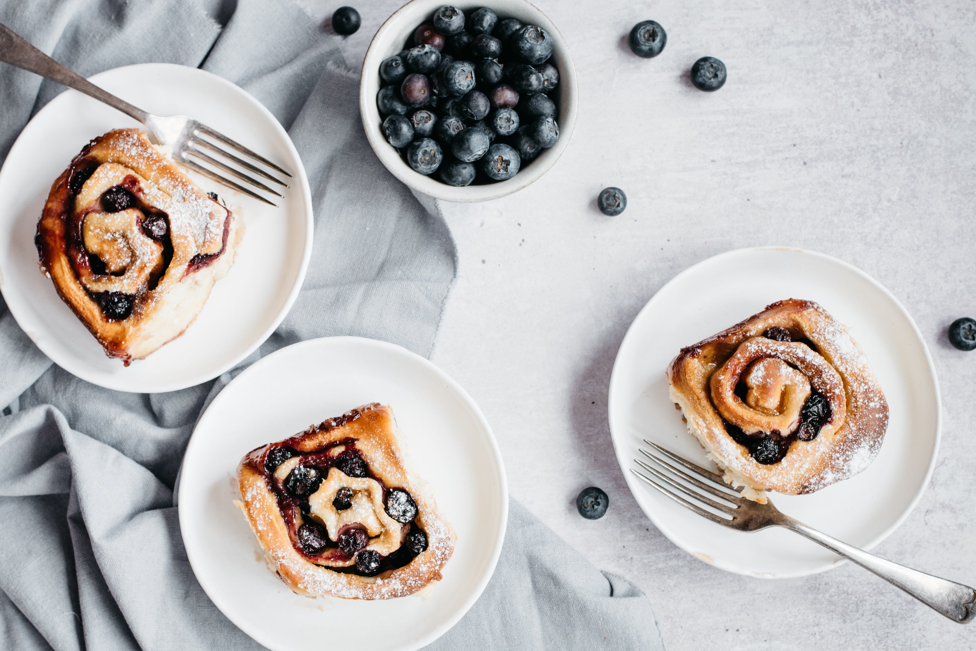 Blueberry & Vanilla Rolls on plates, with grey cloth and blueberries in a bowl