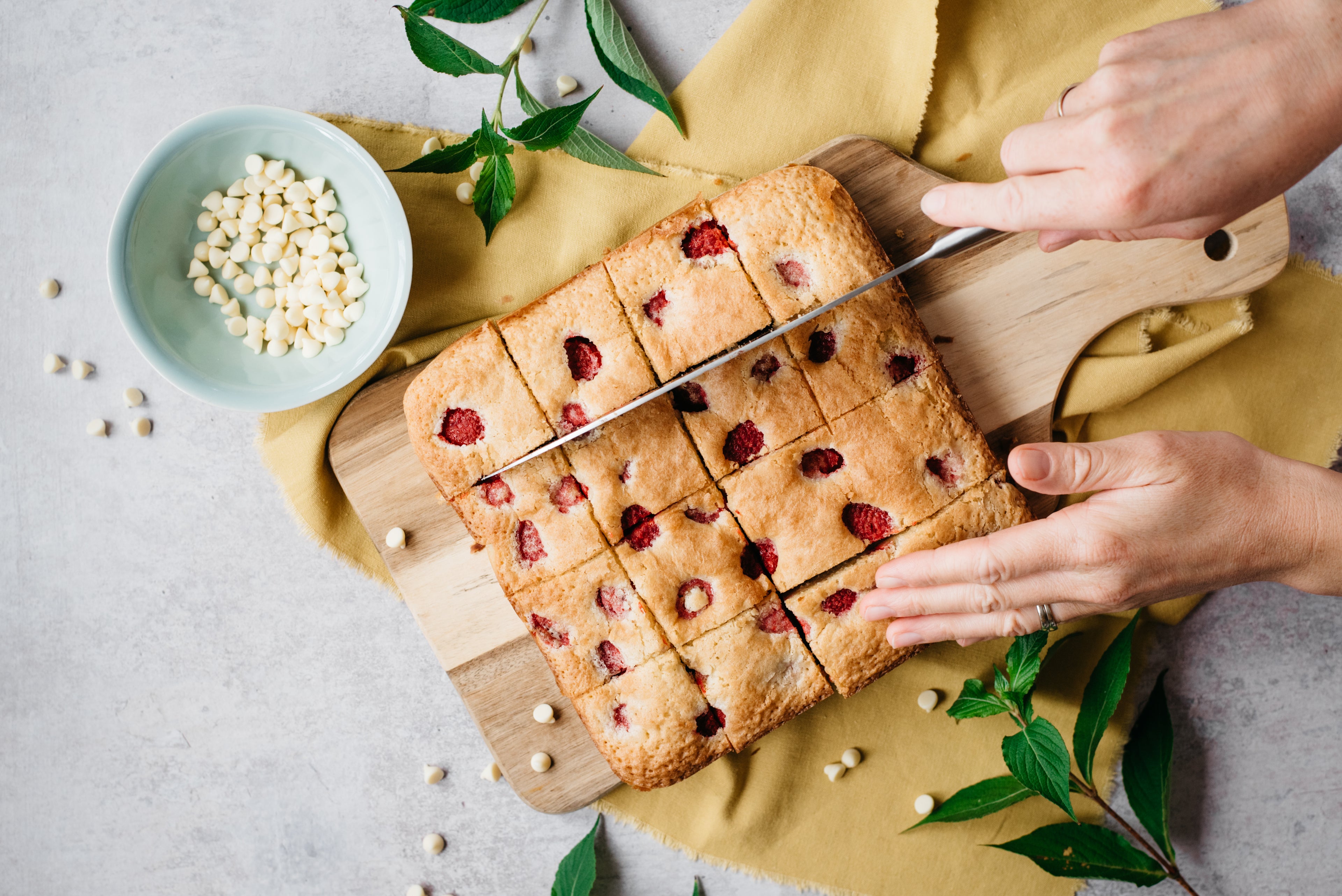 Top down view of a hand holding a knife slicing into a batch of blondies