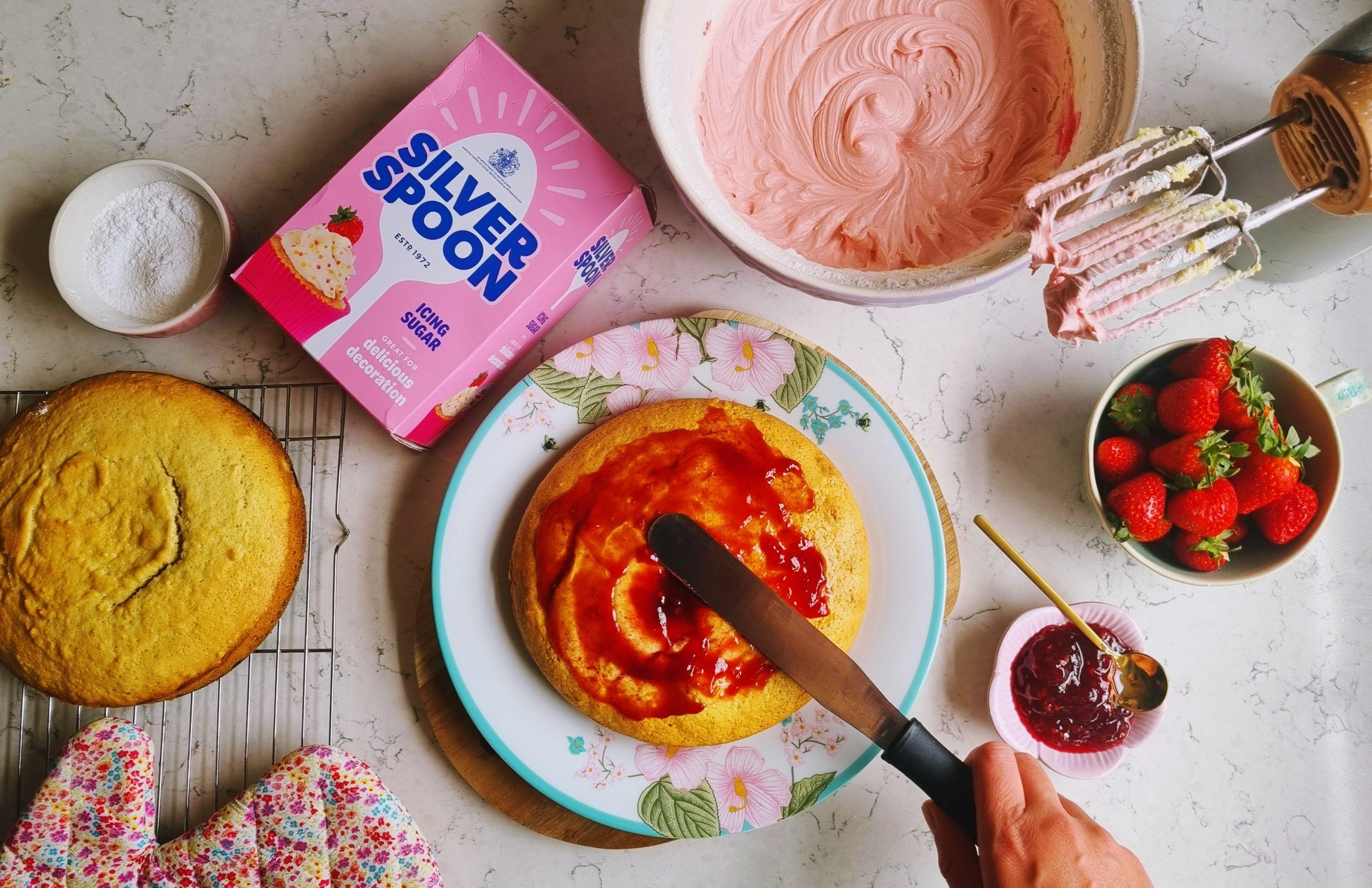 Spreading a thick layer of raspberry jam inside a strawberry sponge cake 