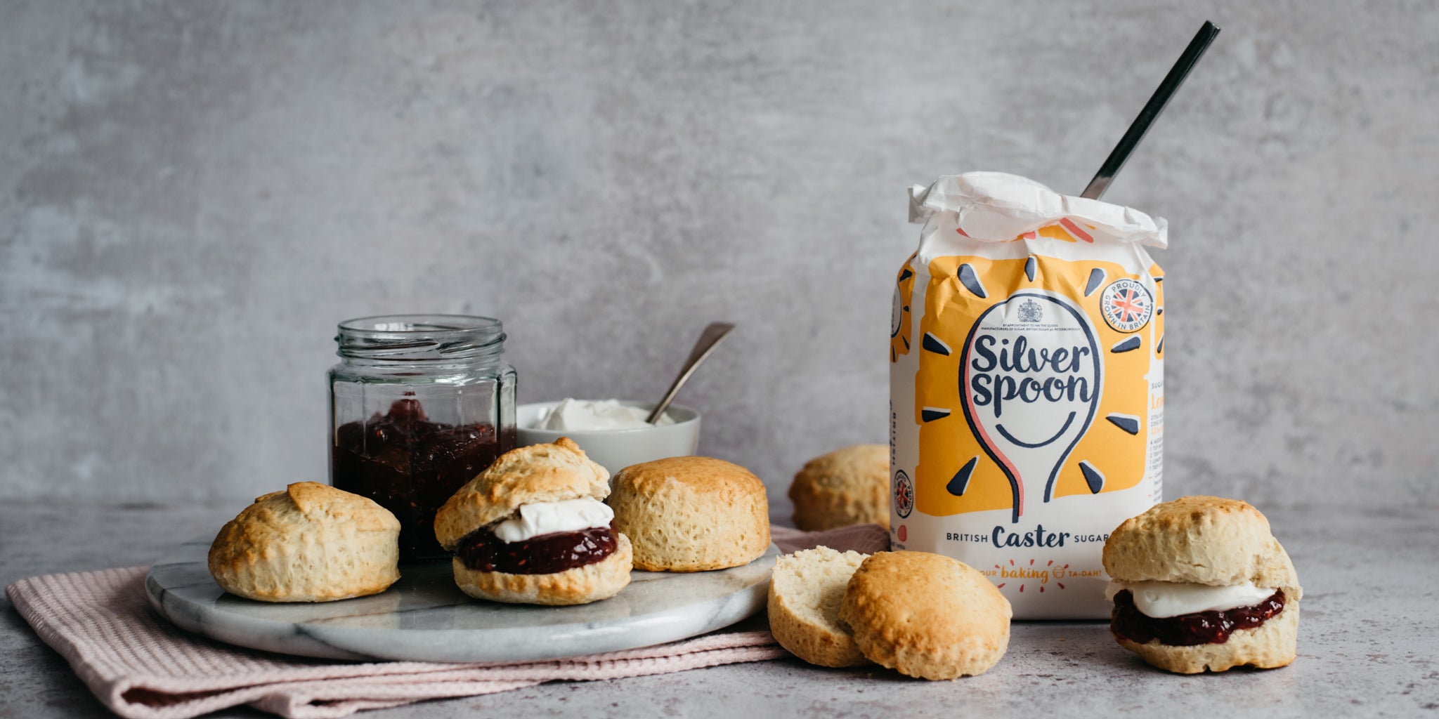 Vegan Scones served cut in halves with plant based cream and jam - next to a bag of Silver Spoon Caster Sugar