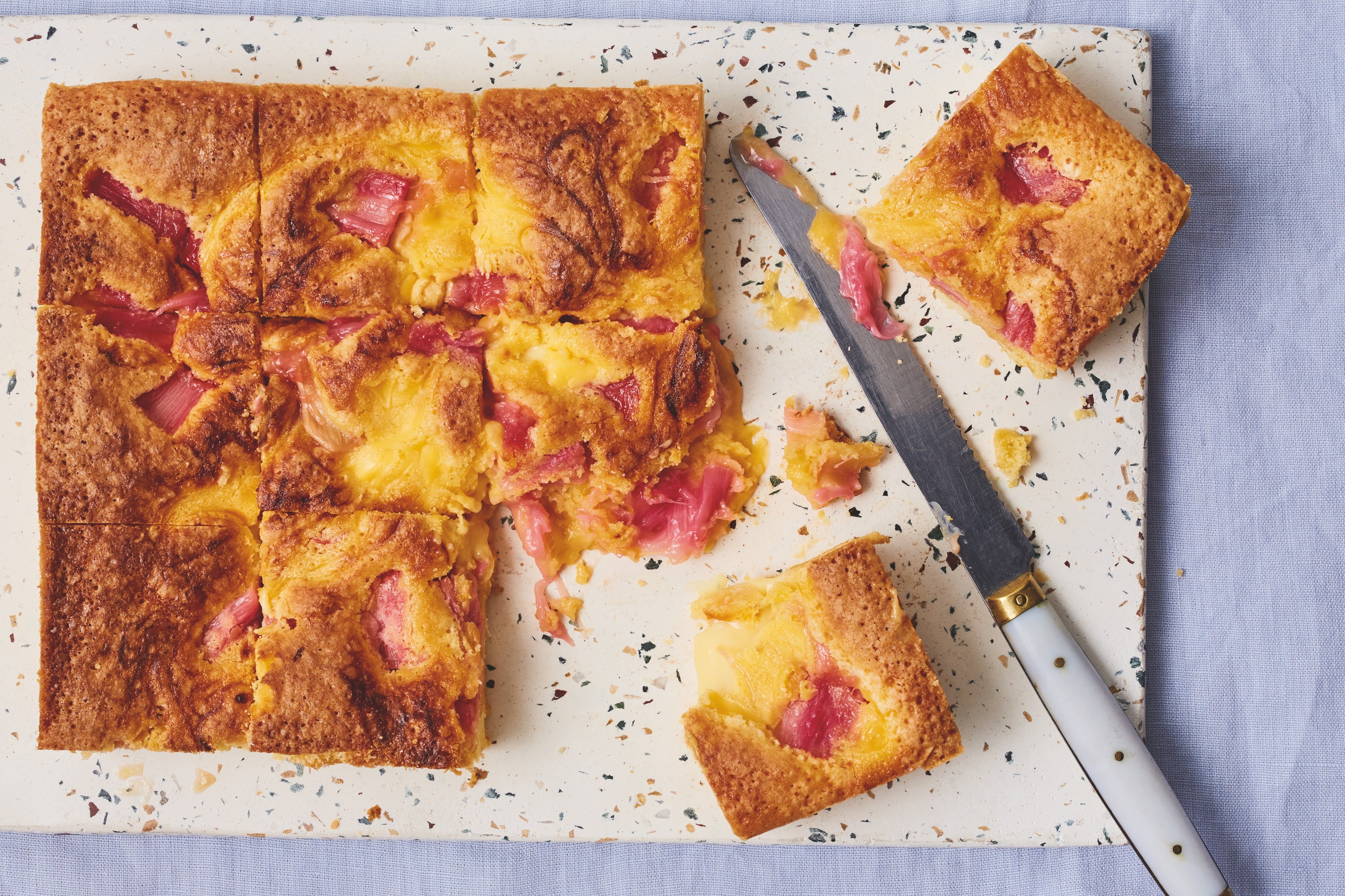 Rhubarb blondies on white board with knife. Partially cut with two squares pulled apart