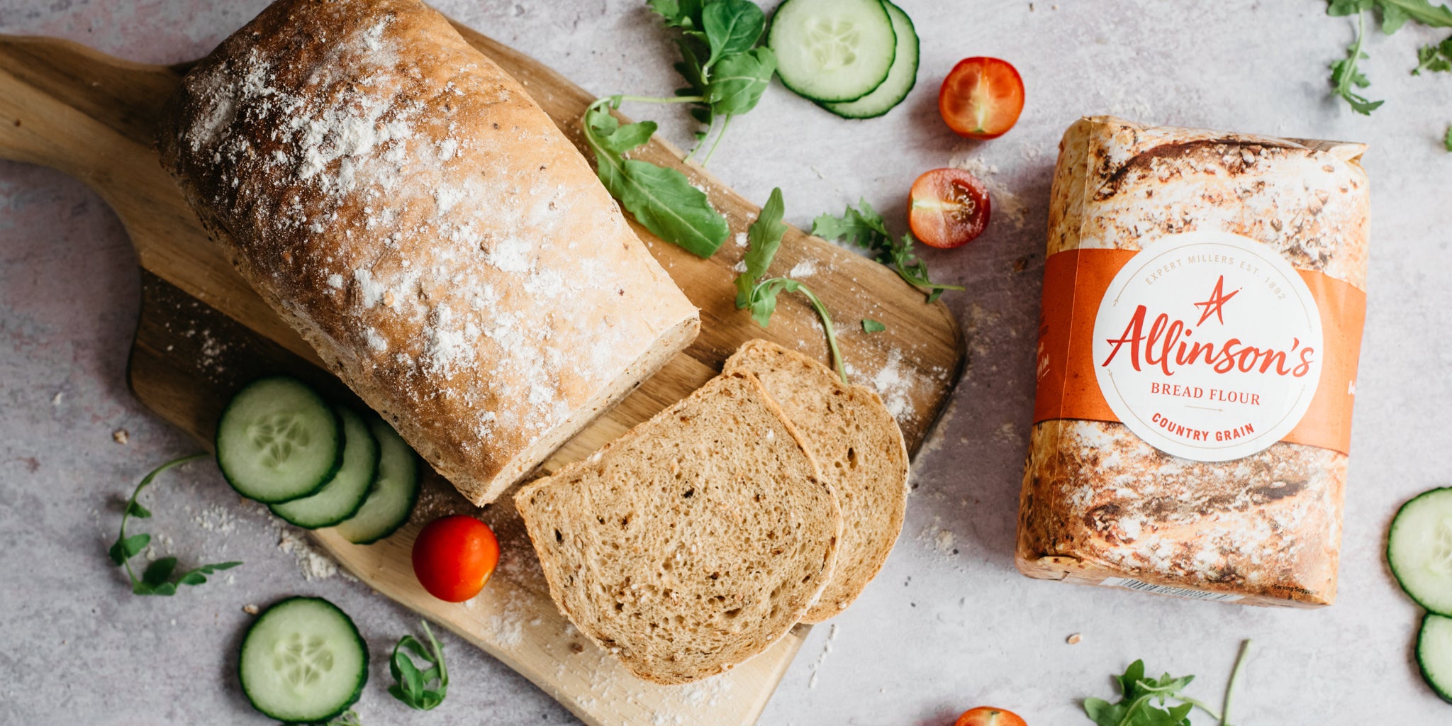 Top view of Farmhouse Country Grain Loaf on a serving board, next to a bag of Allinson's Country Grain Flour and garnished with salad 