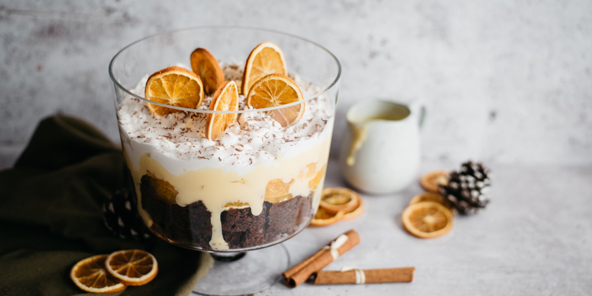 Close up of Chocolate Orange Trifle with slices of orange and sprinkles of chocolate on the top. Jug of Baileys custard in the background
