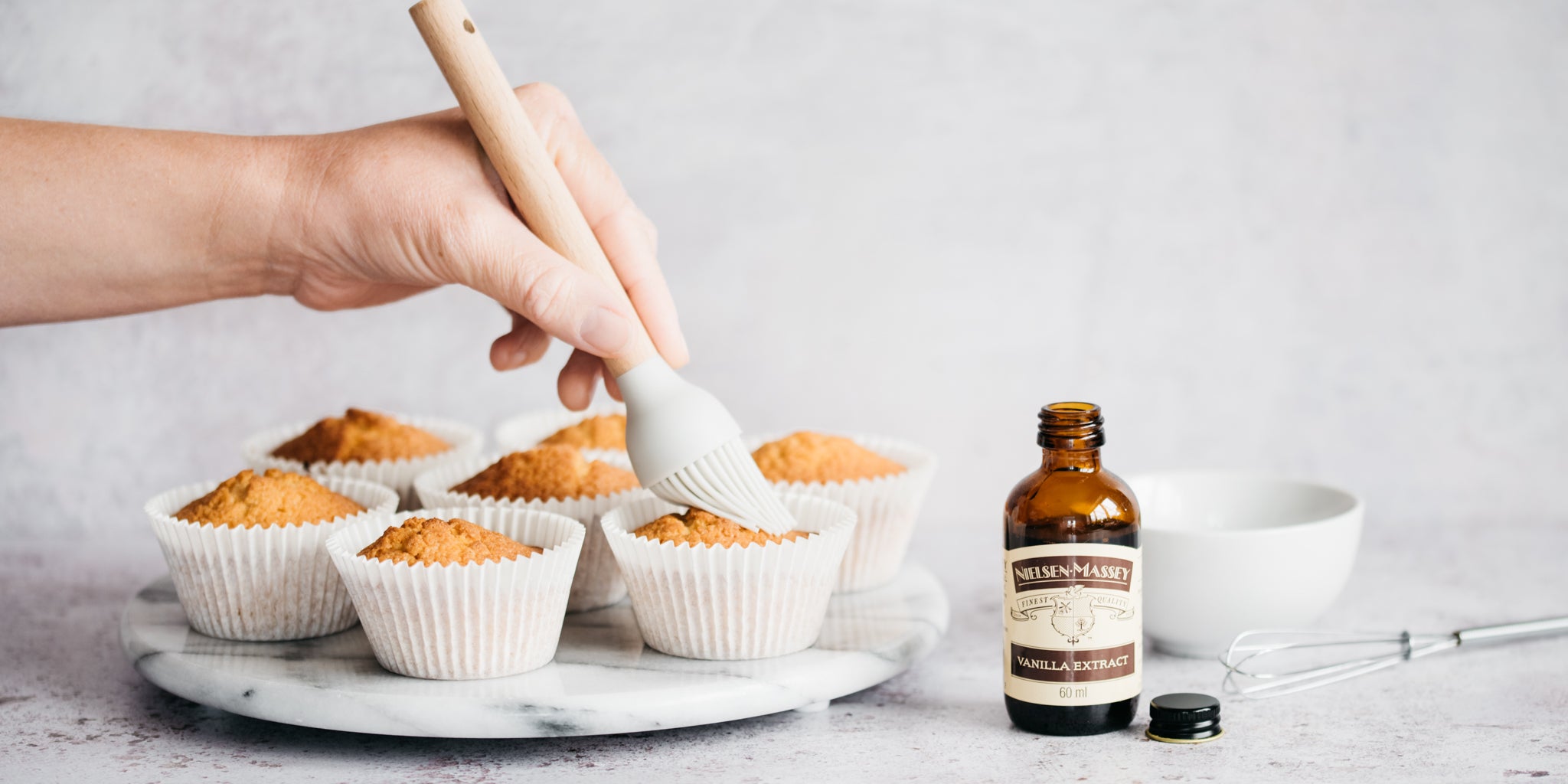Vanilla Extract Cupcakes being hand brushed with Nielsen Massey Vanilla Extract to infuse the sponge