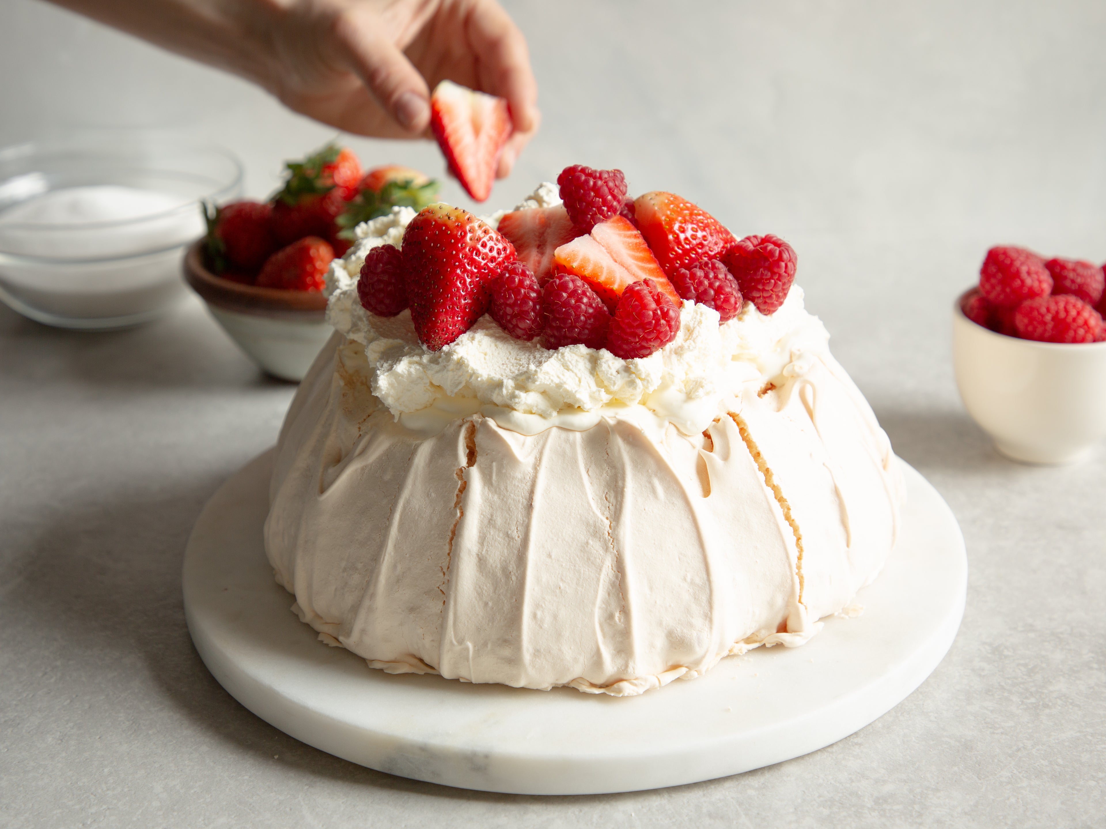 Strawberry Pavlova being hand decorated with fresh strawberries and raspberries on a layer of whipped cream