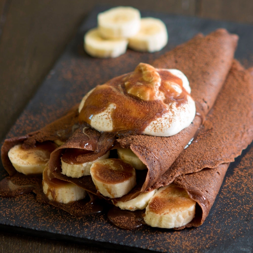 Chocolate pancakes dusted with cocoa powder, topped with sliced bananas and cream