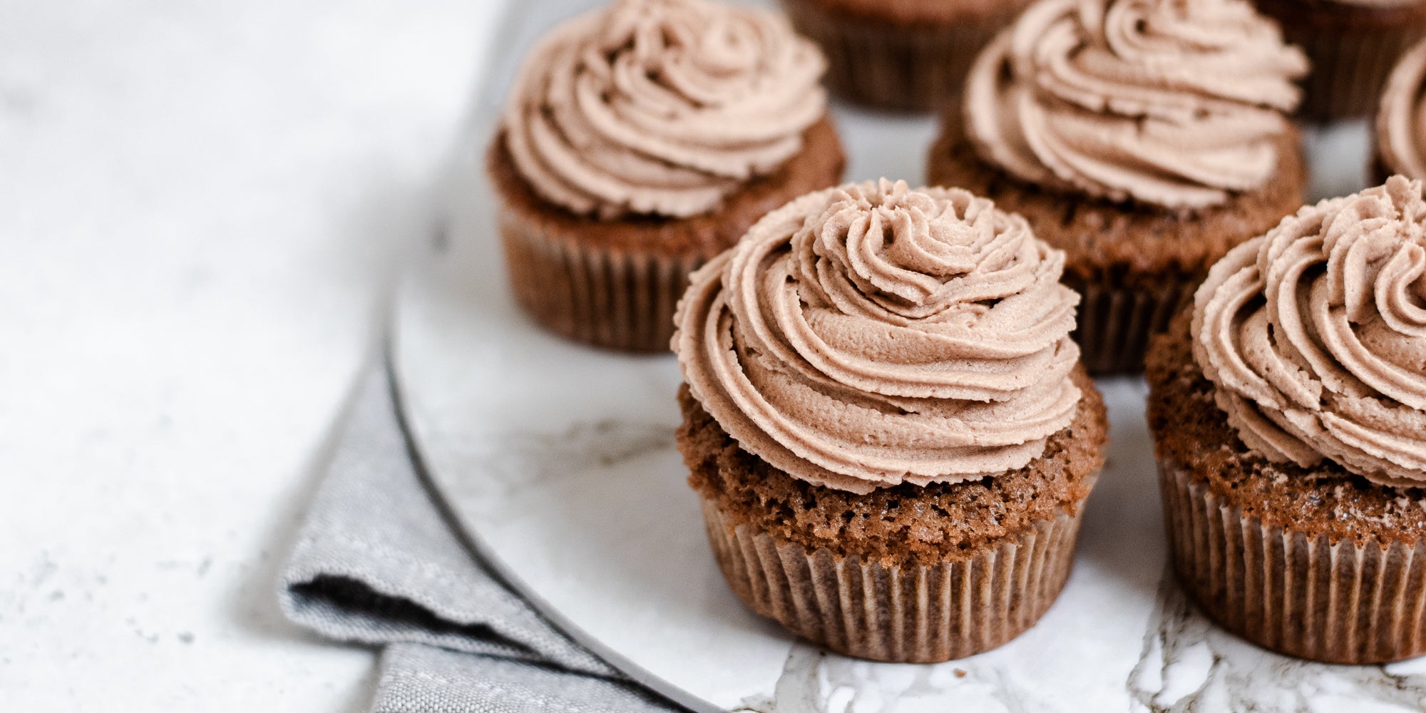 Close up of cupcake topped with Dairy Free Vegan Chocolate Buttercream on a marble serving plate