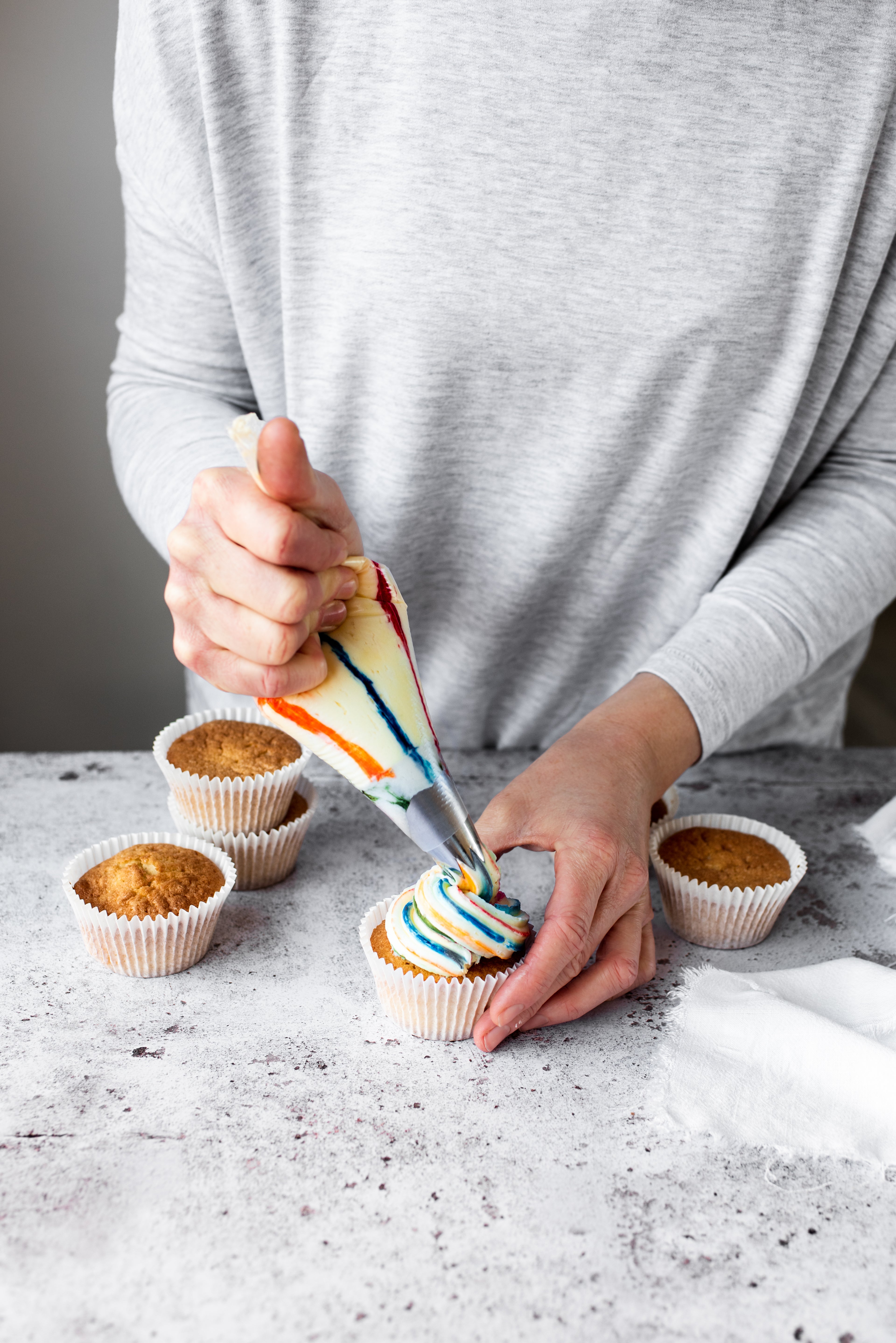 Female piping rainbow icing onto cupcake