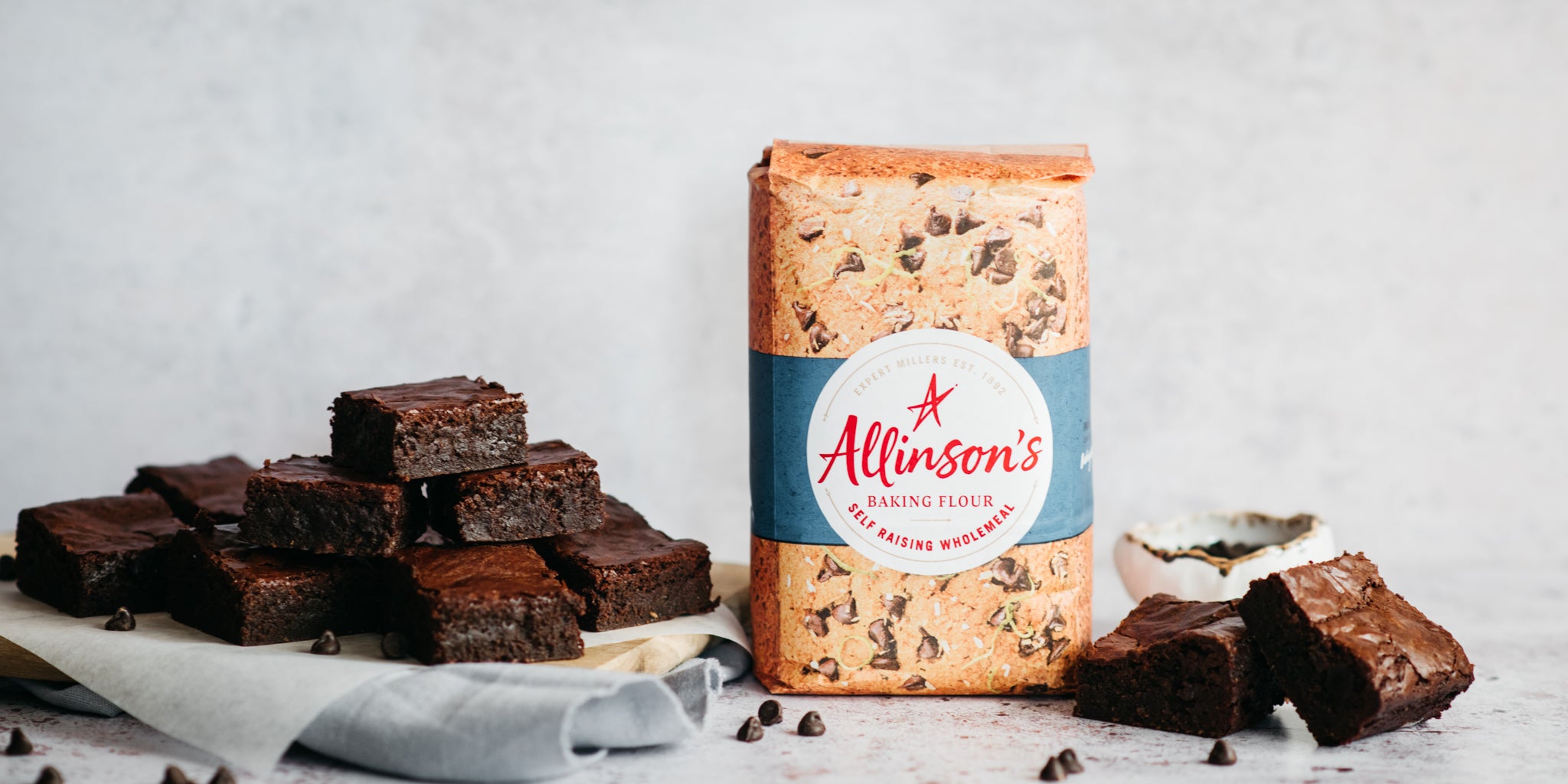 A batch of Wholemeal Chocolate Brownie chopped into squares served on parchment paper, next to a bag of Allinson's Wholemeal flour