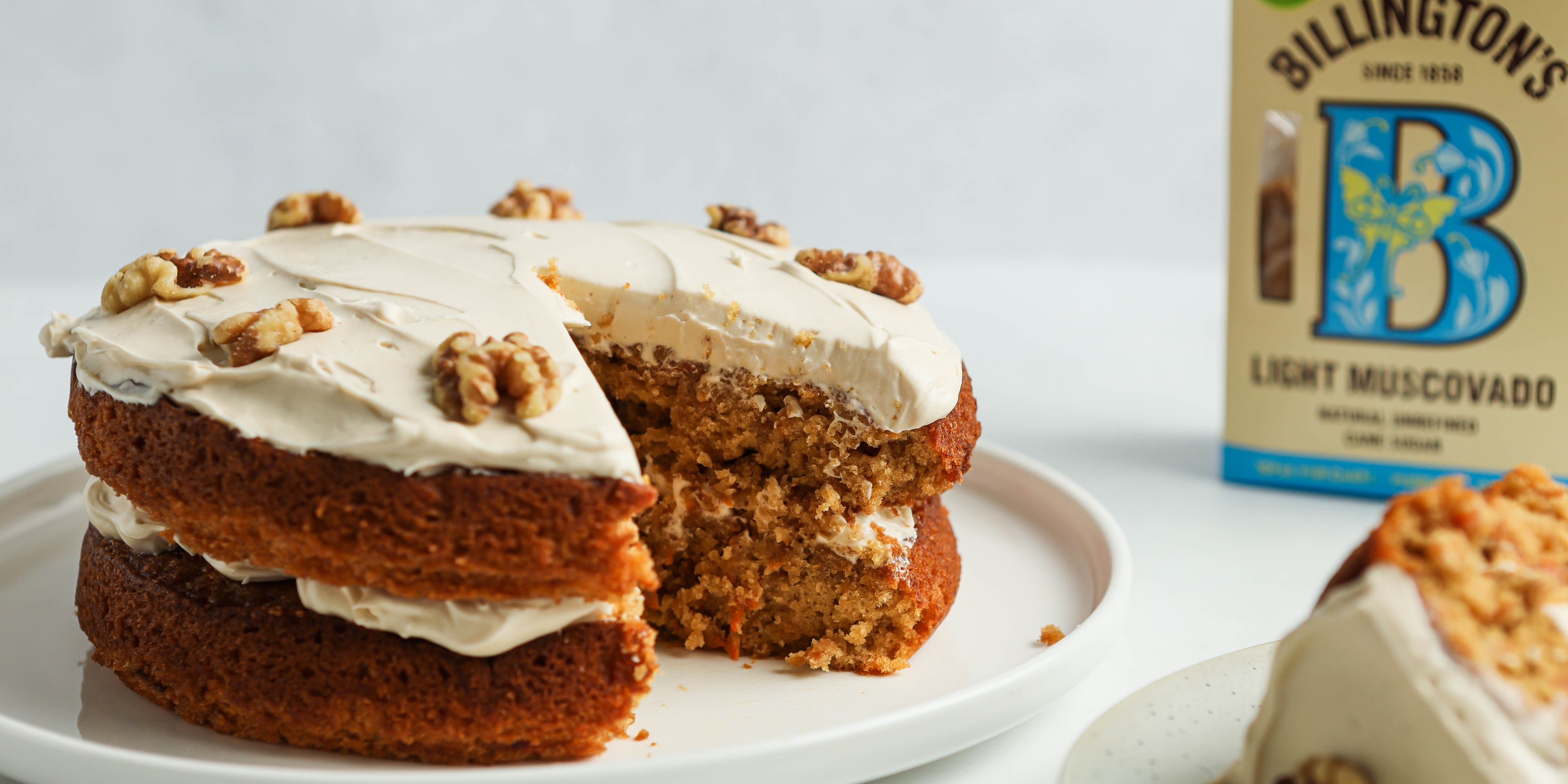 Classic Carrot Cake close up, with a slice cut out of it next to a box of Billington's Light Muscovado Sugar