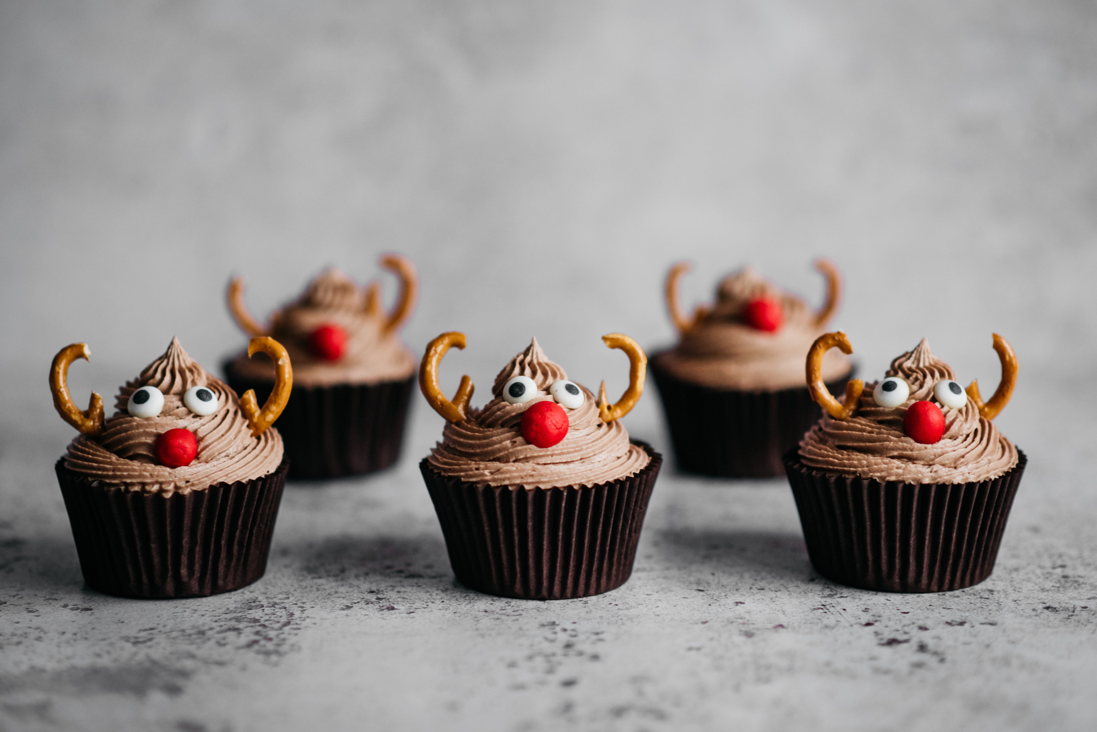 A batch of Reindeer Cupcakes decorated with pretzel antlers, icing eyes and red sweetie noses