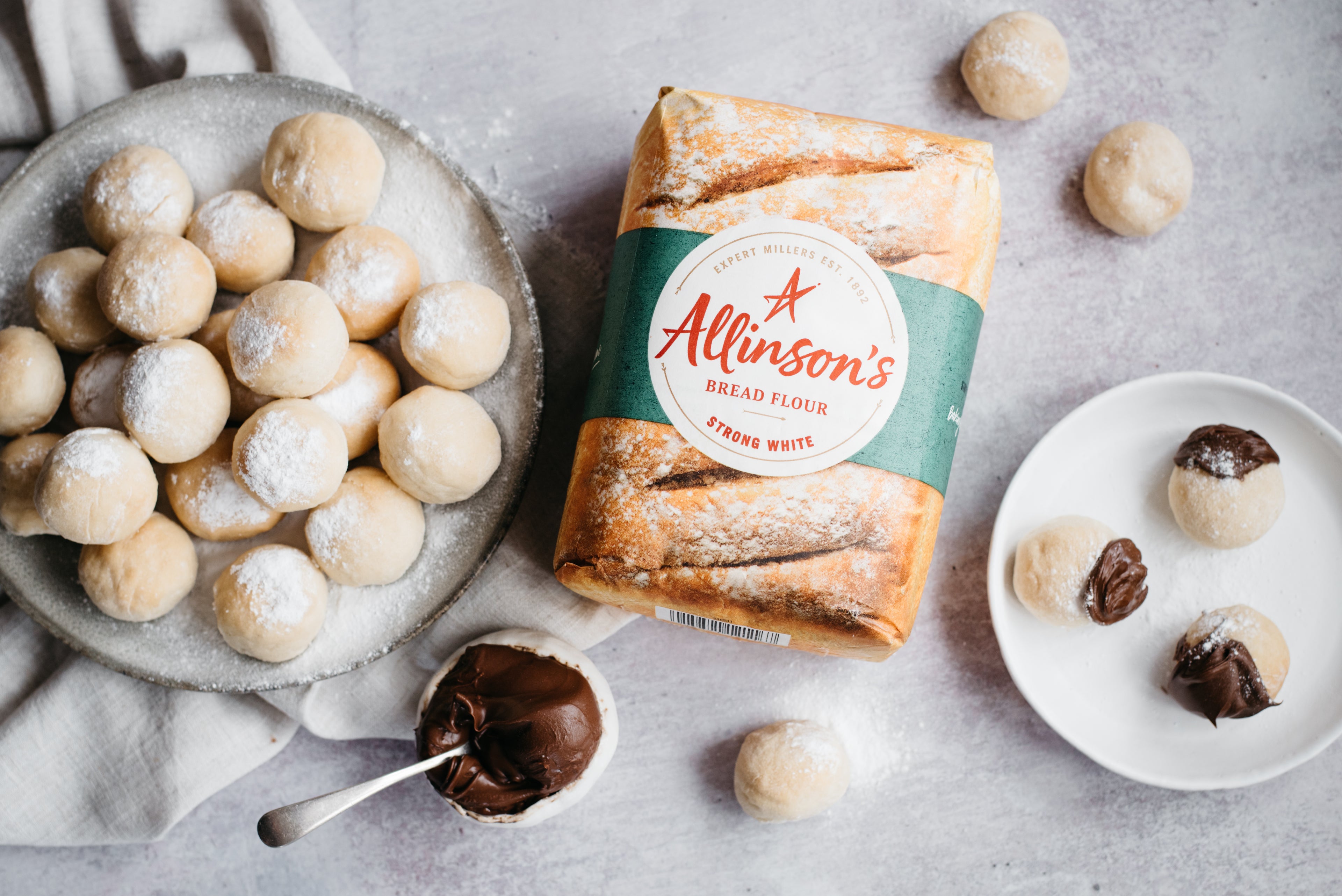 Top view of Chocolate Dough Balls with a bowl of chocolate sauce next to a bad of Allinson's strong white flour, with a plate of dough balls dipped in chocolate