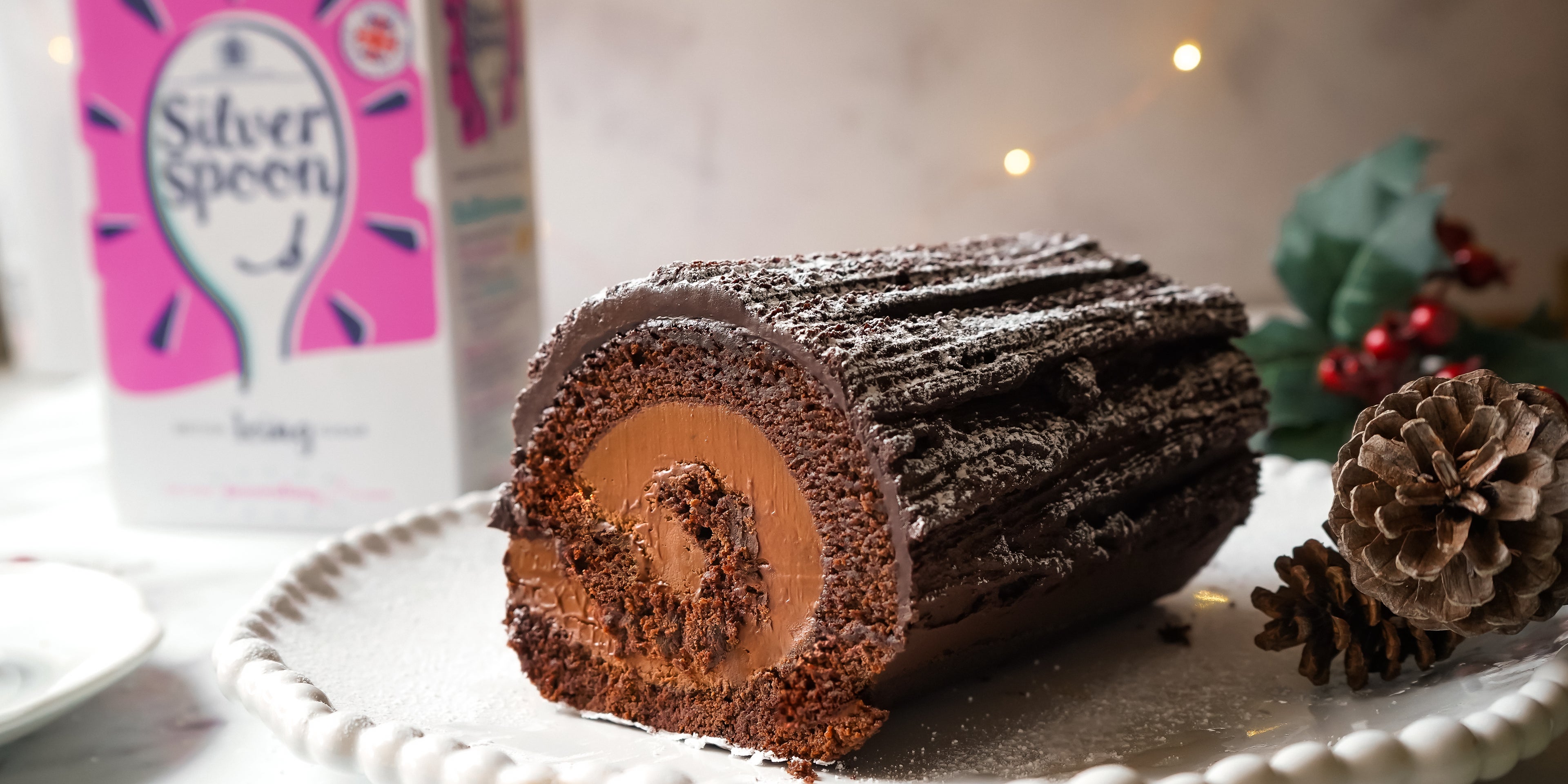 Close up Vegan Yule Log dusted in Silver Spoon icing sugar, with a box of Silver Spoon icing sugar in the background