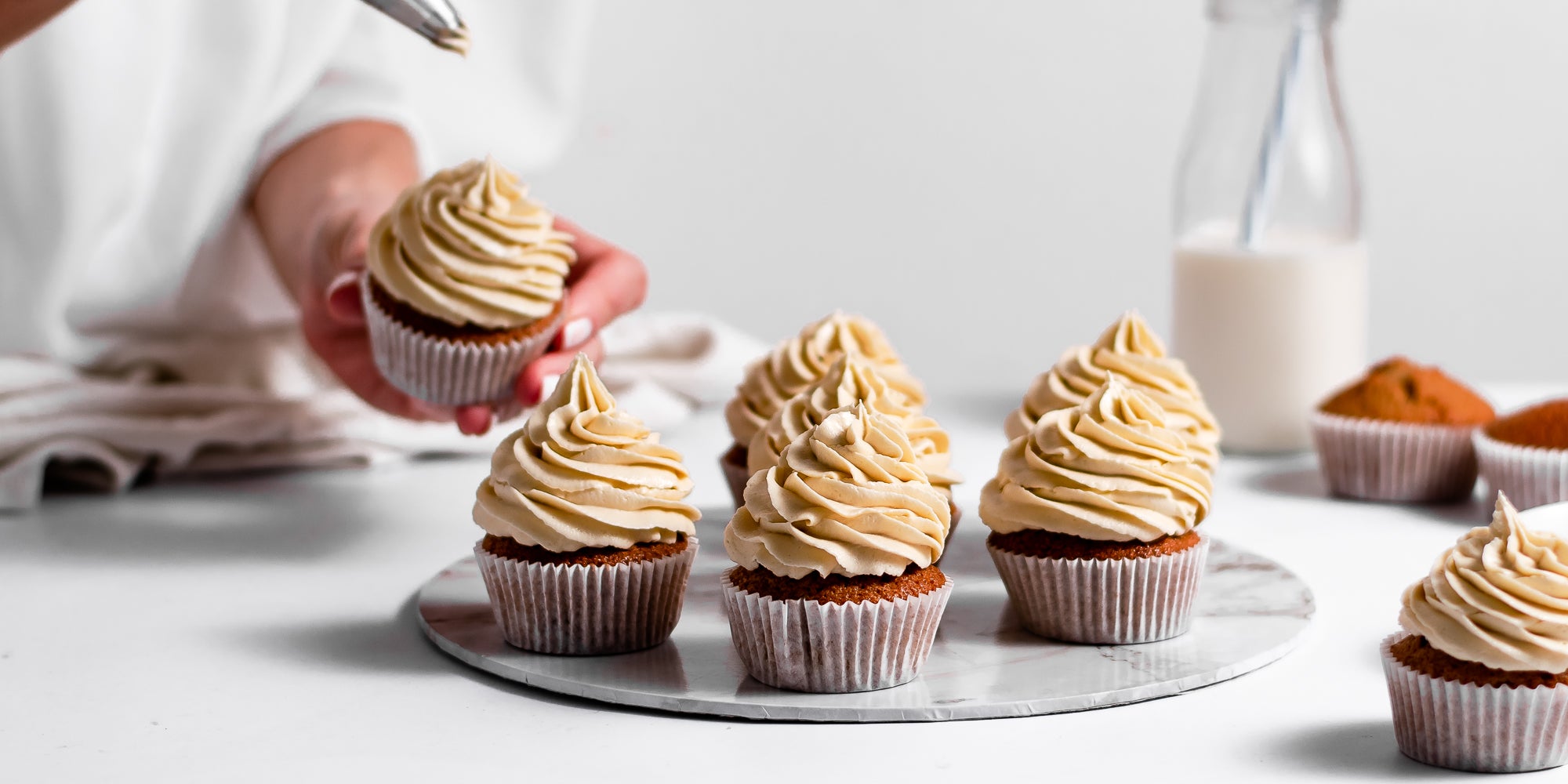 Gingerbread Cinnamon Cupcakes on a plate, being hand decorated with caramel buttercream.