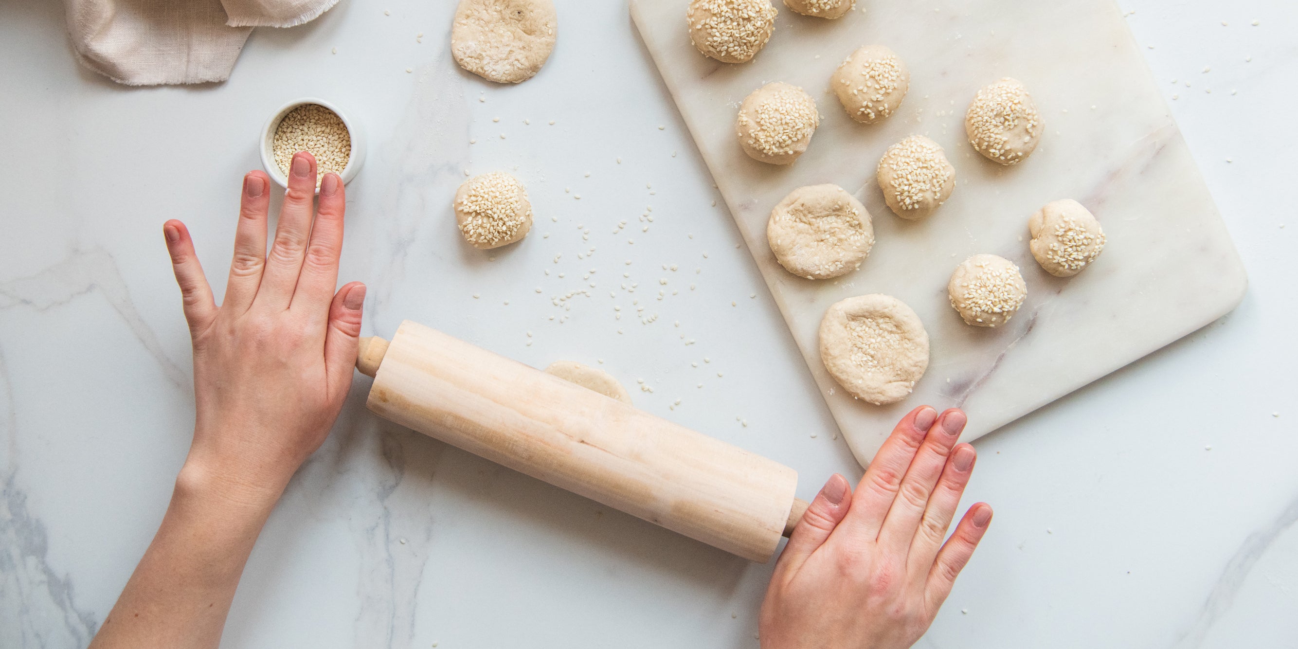 Dough balls of Bánh Tiêu being rolled out by a hand holding a rolling pin