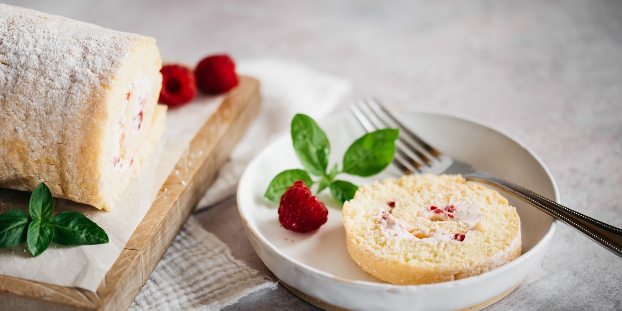 Raspberry roulade with slice removed on white plate beside with a fork and raspberries